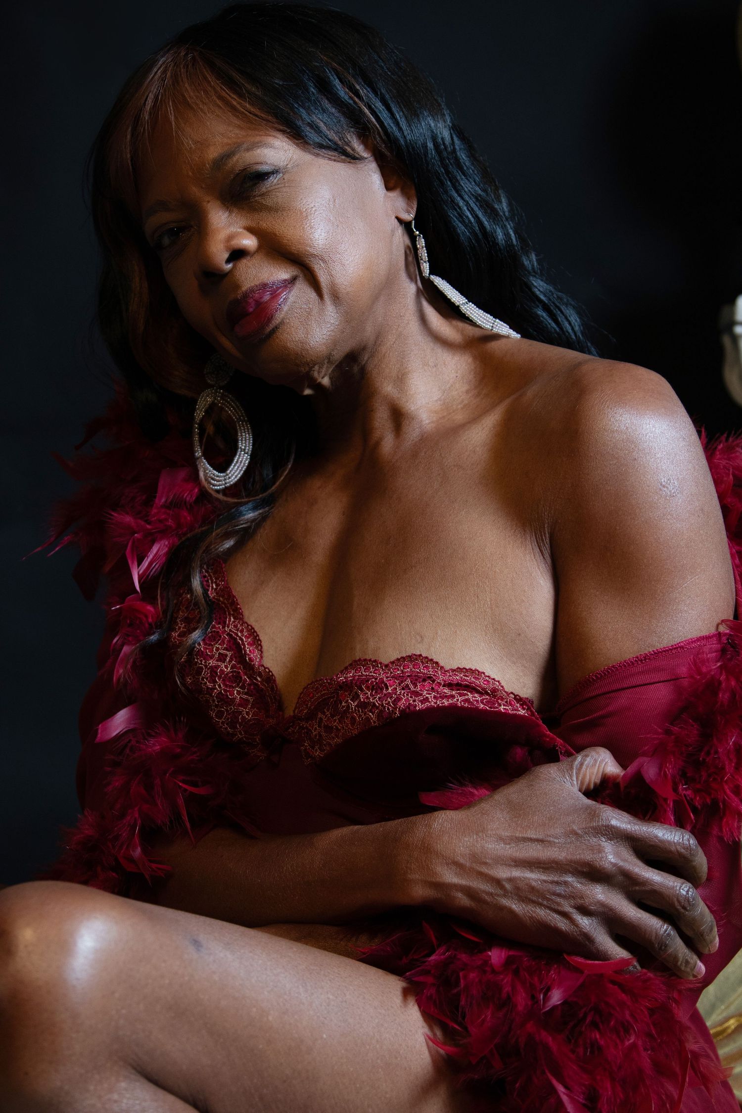 Elegant woman in red lace lingerie with feather boa posing in a dramatic studio portrait.