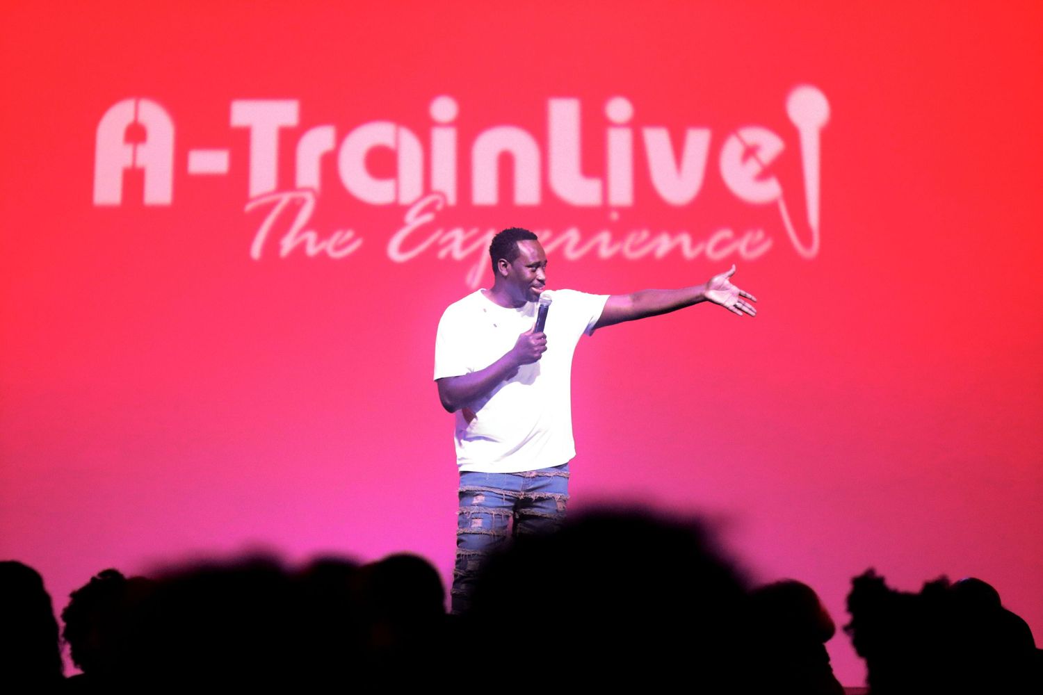 Performer on stage at A-Train Live The Experience event gesturing to crowd under red lighting.