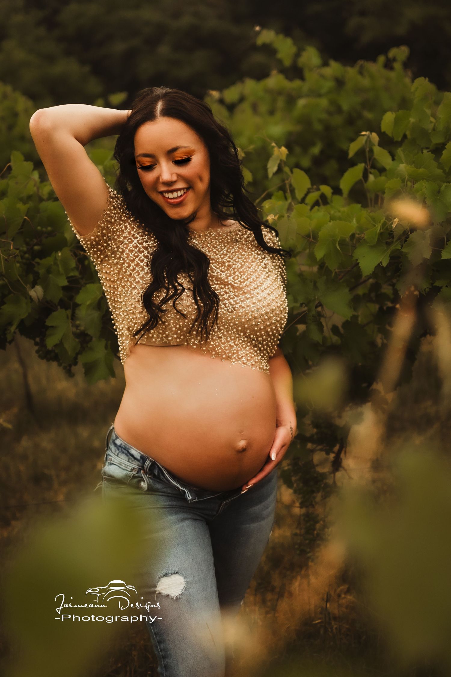 Joyful maternity moment captured in a sunlit vineyard wearing a gold sequined top.
