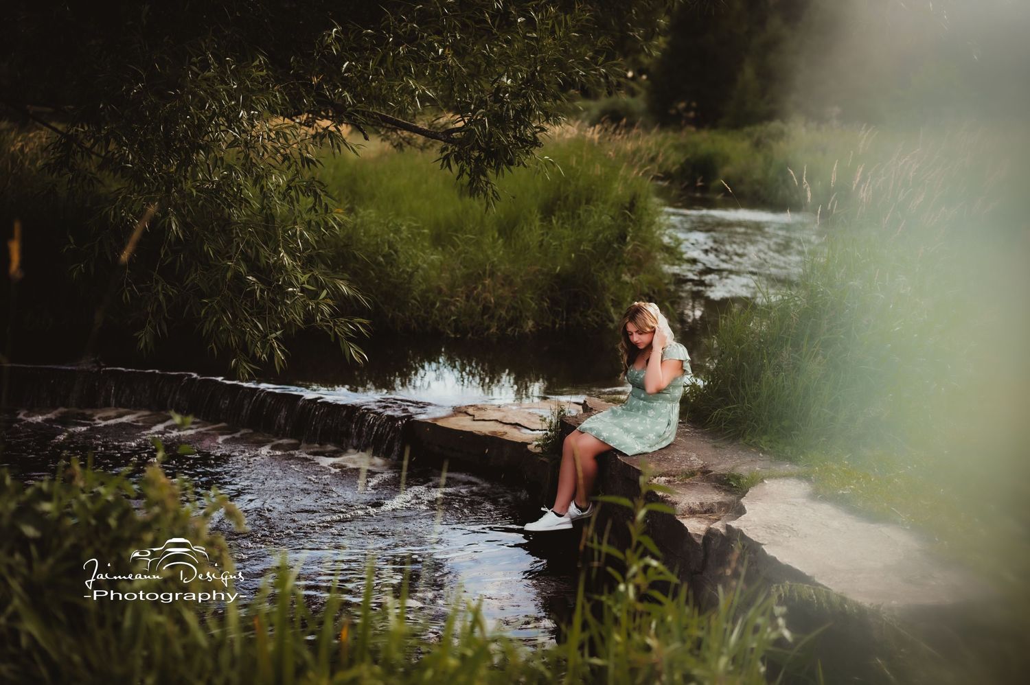 Scenic outdoor photo by a stream with someone sitting on rocks in a mint dress.