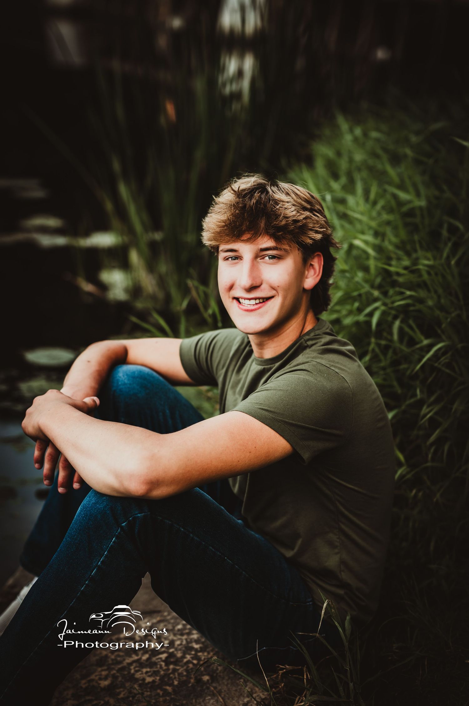 Casual portrait by pond with natural greenery in background.