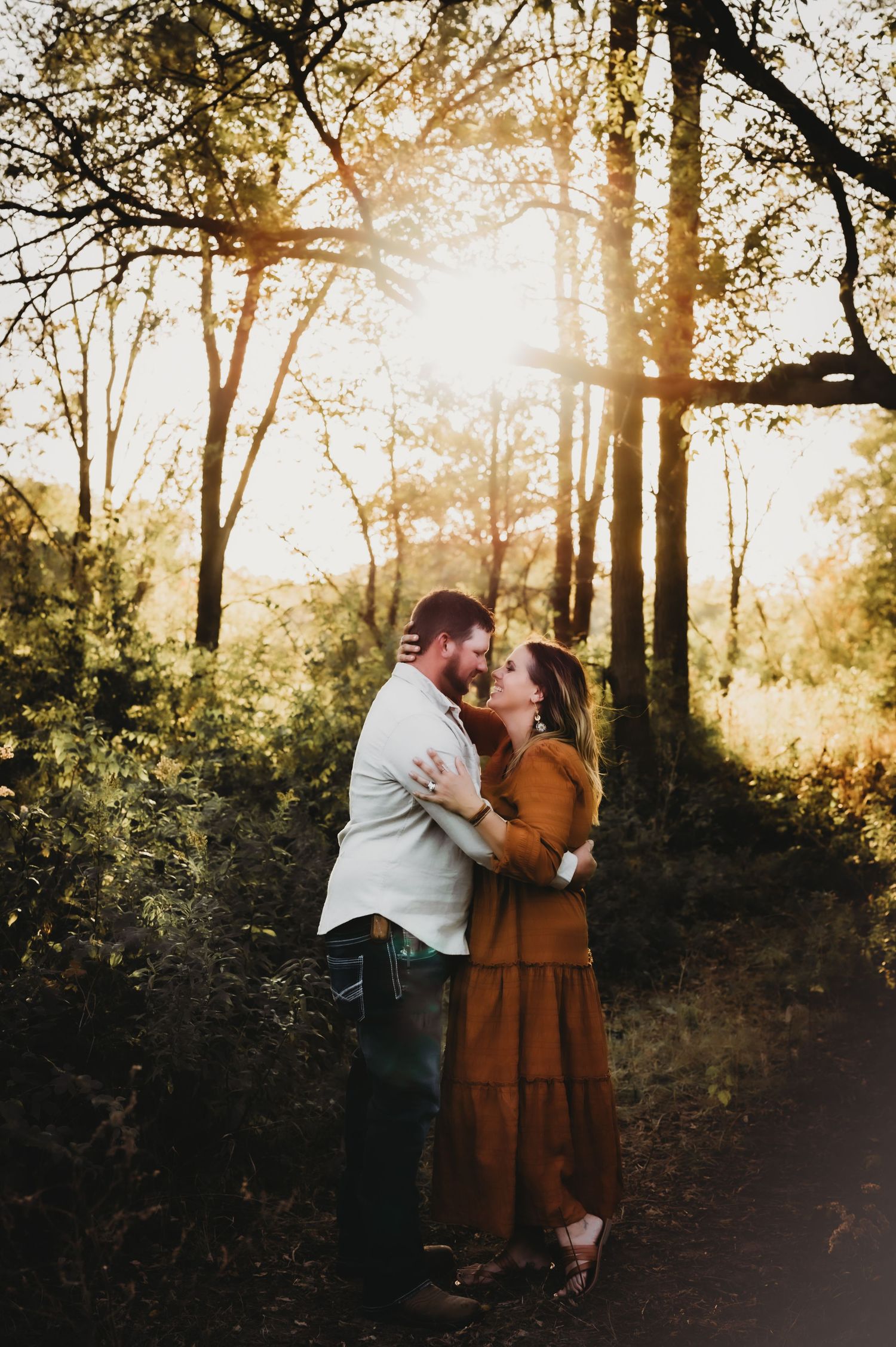 A romantic couple embraces on a forest path during golden hour as sunlight filters through autumn trees.