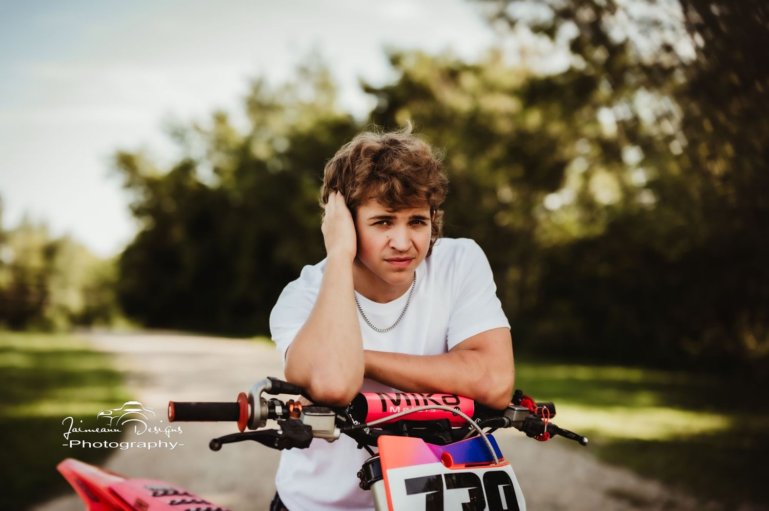 Casual portrait of someone sitting on a red dirt bike in a sunny outdoor setting.