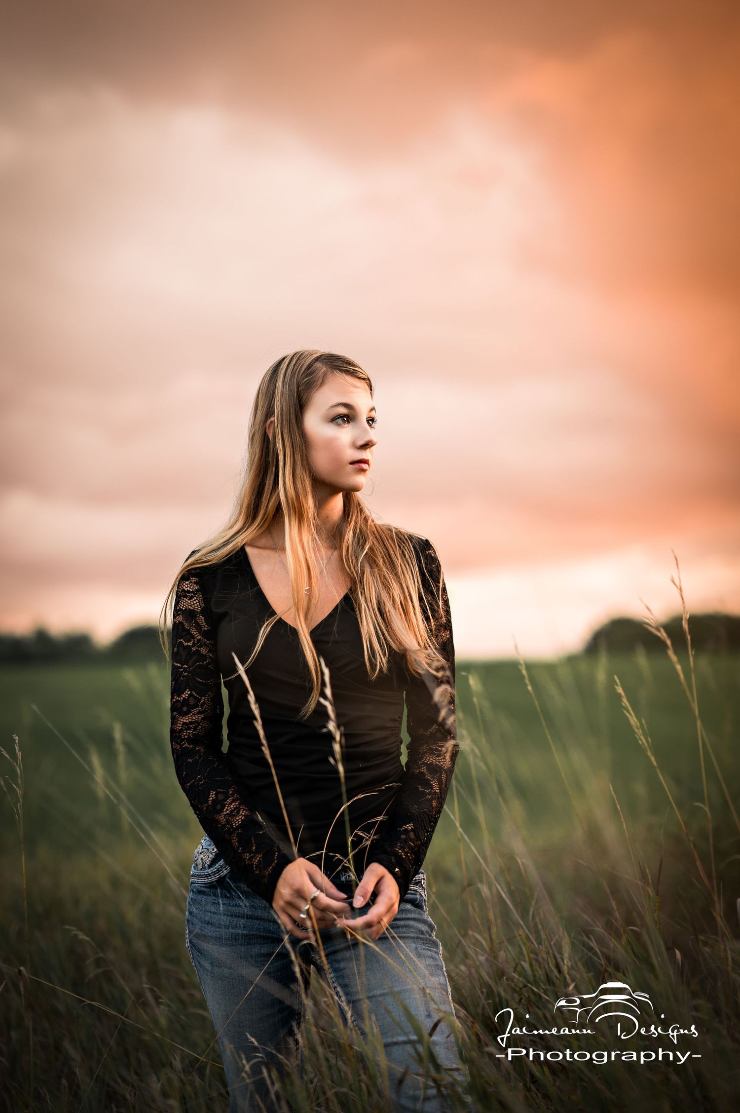 Portrait session in tall grass field during golden hour with dramatic orange sky.