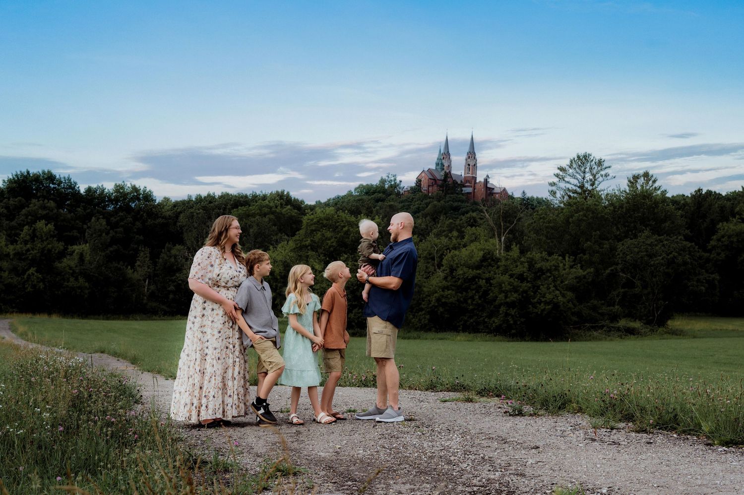 Family of six poses on a gravel path with lush greenery and a historic cathedral at dusk.