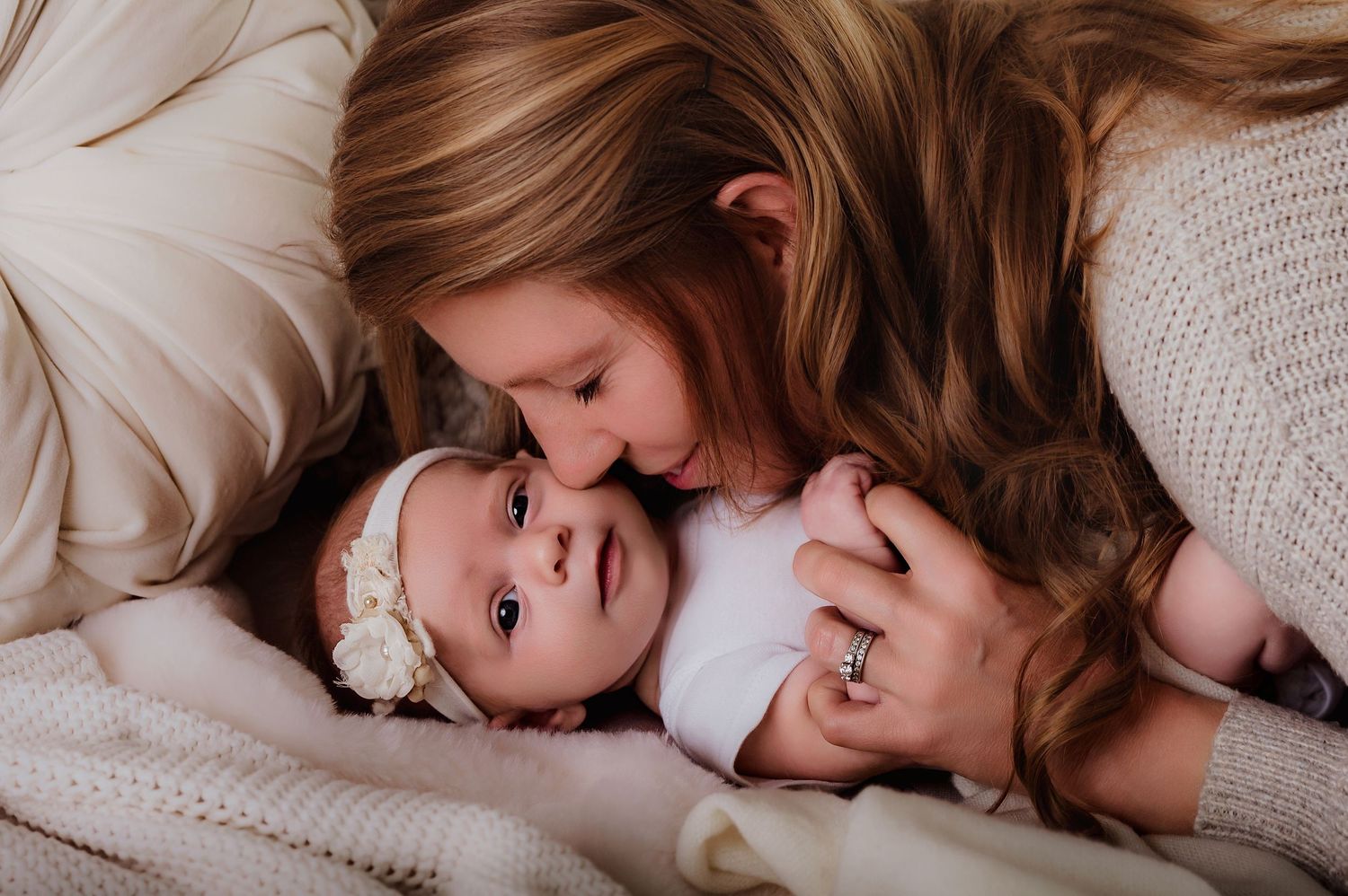 A tender moment as a mother leans down to kiss her newborn baby wearing a white floral headband.