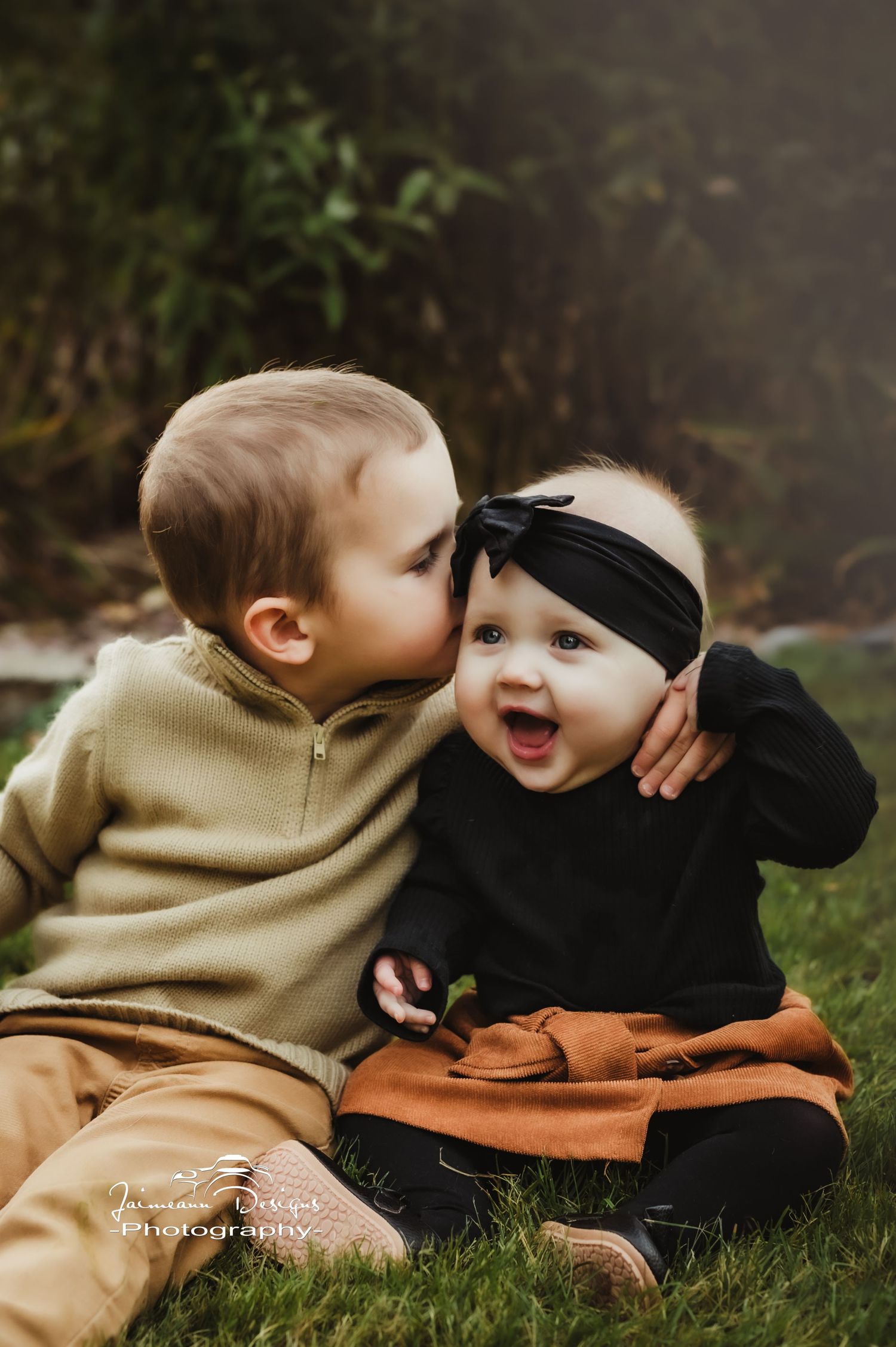 Two small children share a sweet moment on the grass during autumn.