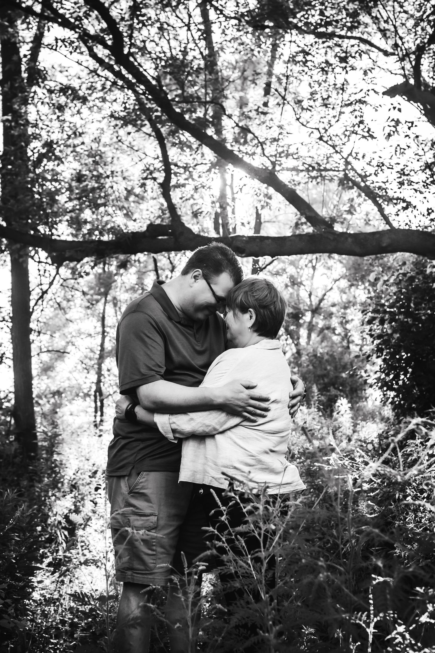 A loving couple shares an intimate moment surrounded by trees in a black and white forest scene.