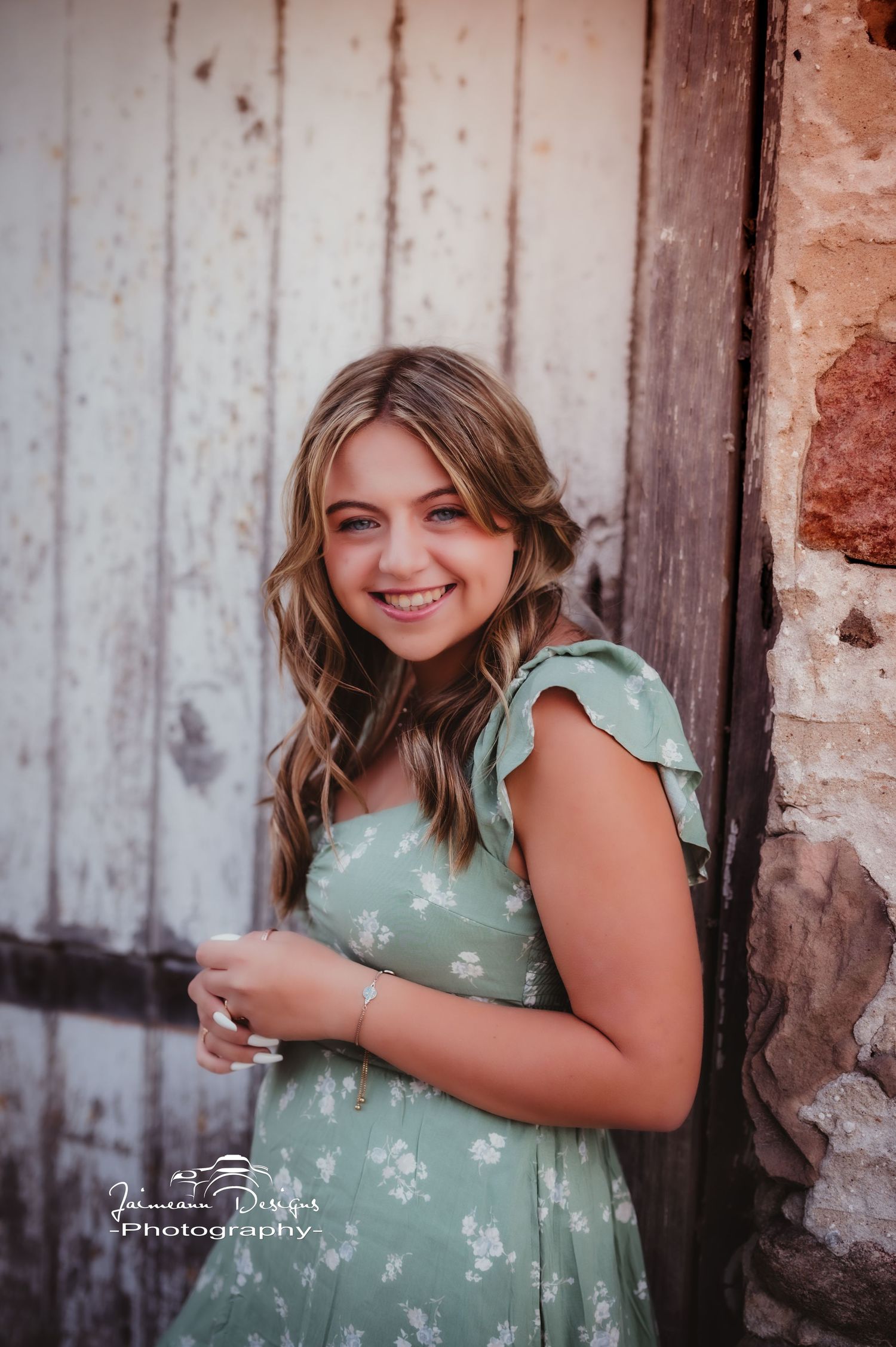 A cheerful pose against a rustic backdrop wearing a sage green flutter-sleeve dress.