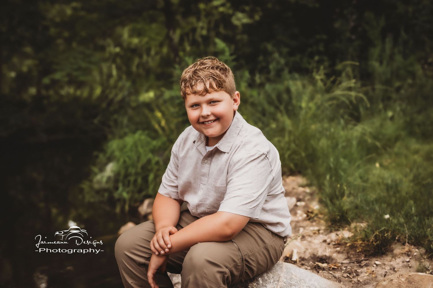 A cheerful individual in casual attire sits on a rock outdoors during a photo session.