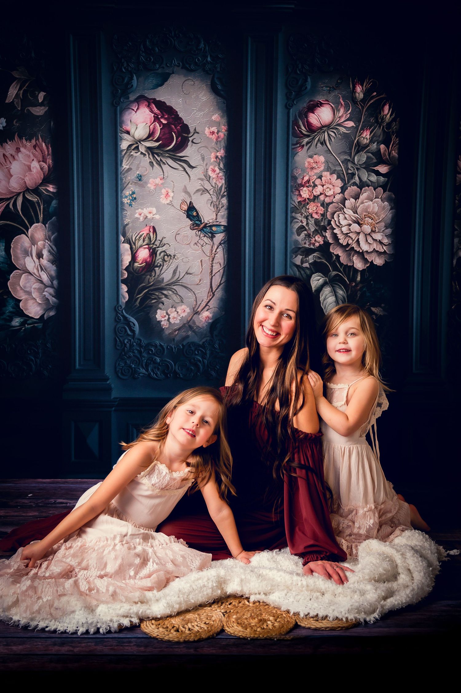 Elegant portrait against floral backdrop with burgundy and cream dresses on plush white fabric.