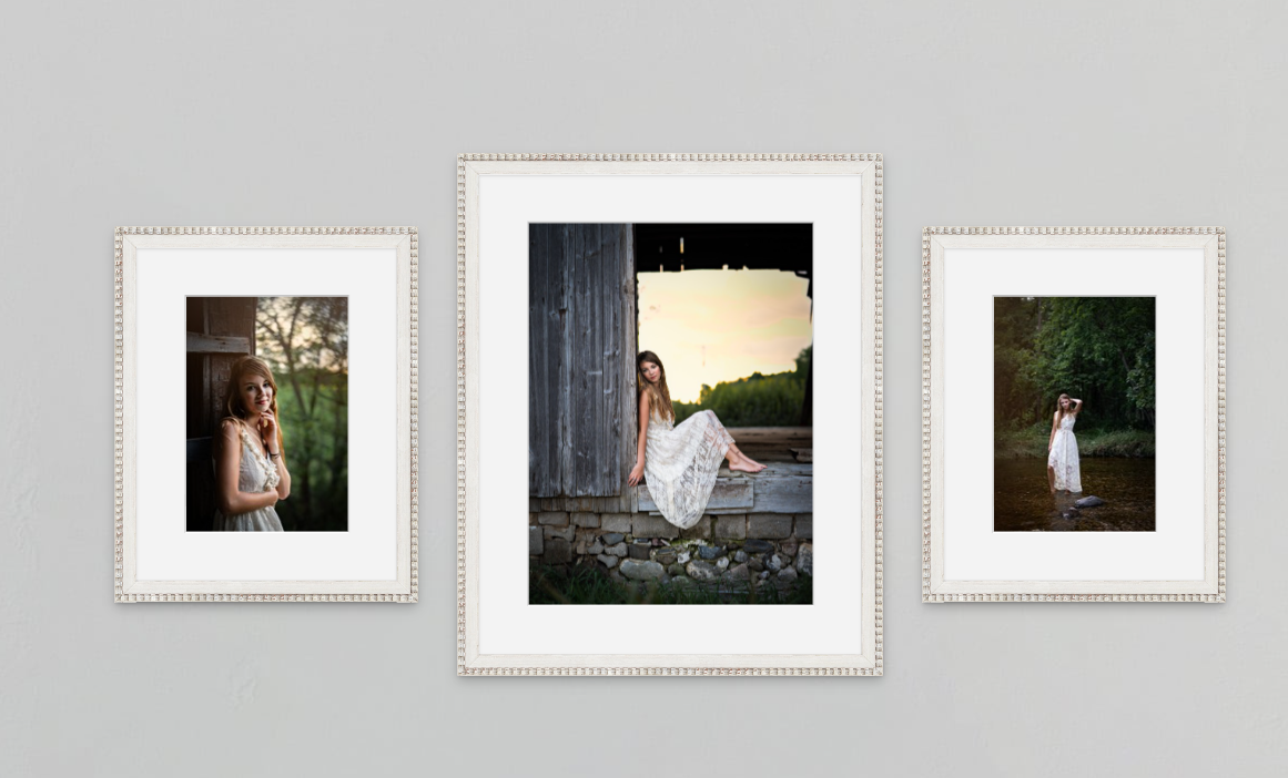 Three framed portrait photos of a young woman in a white dress displayed on a gray wall in elegant silver frames.