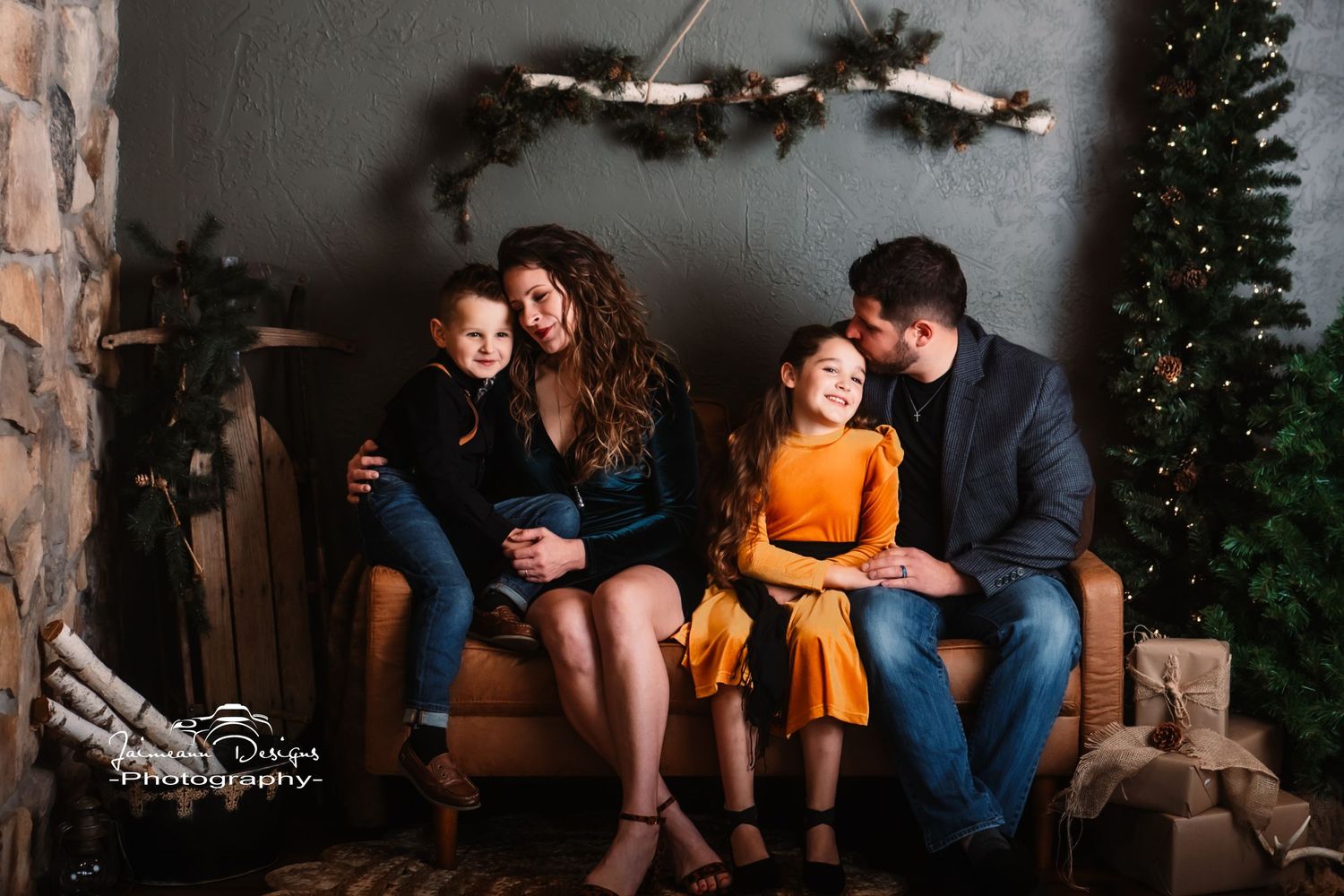 Intimate family photo on brown leather couch with holiday decorations and greenery.
