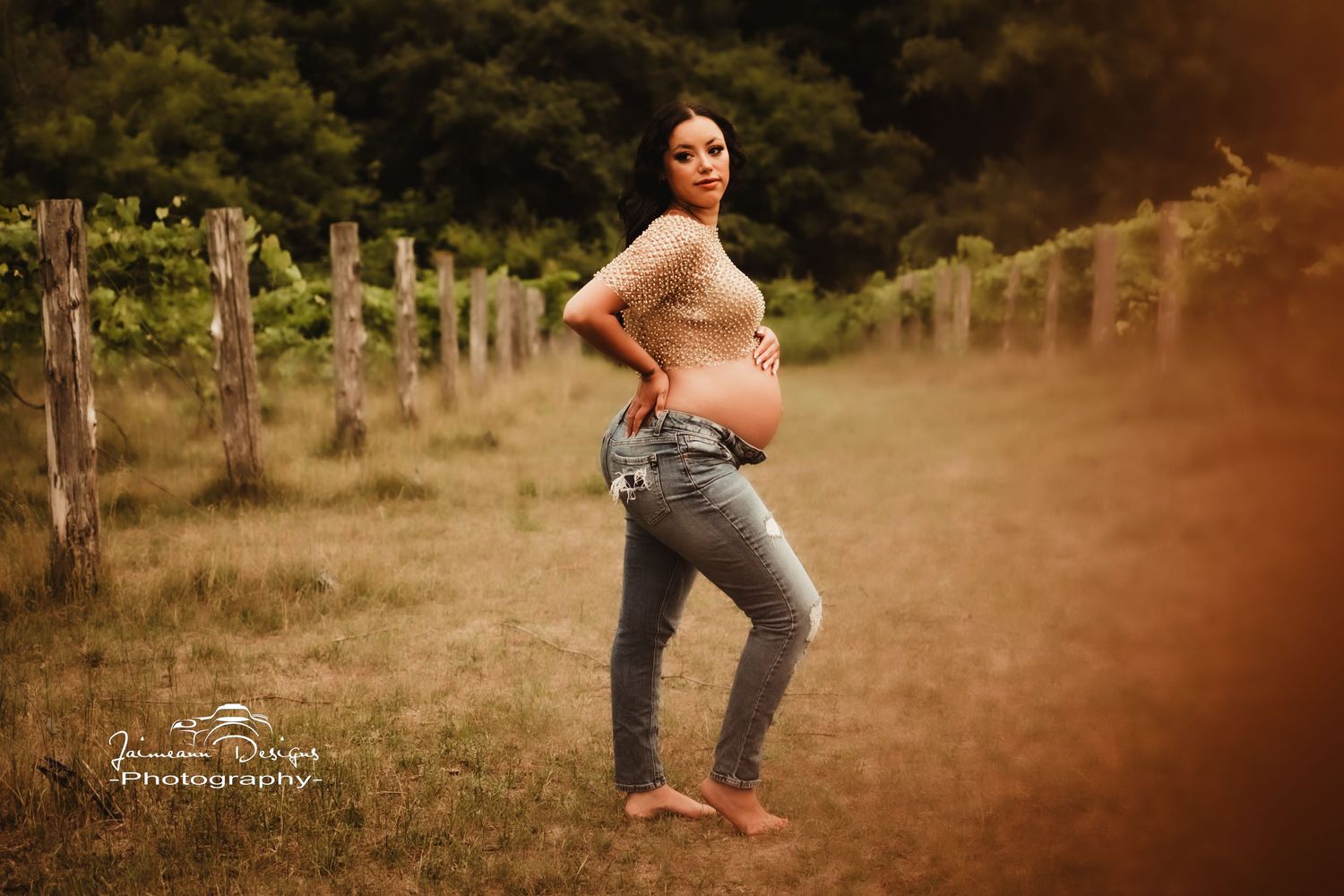 Casual maternity portrait in front of vineyard posts at golden hour.