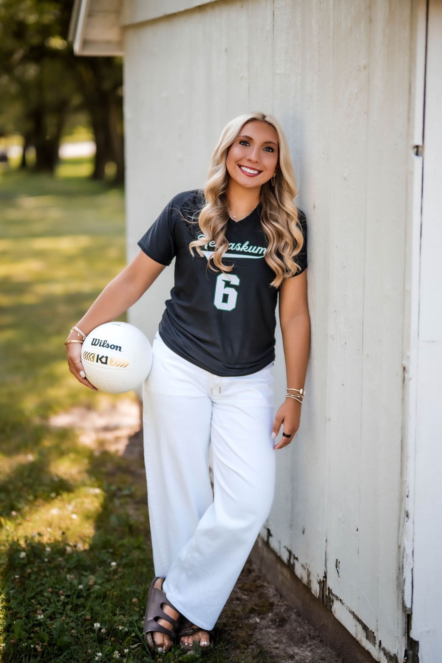 Senior volleyball portrait of a girl holding a volleyball against a white barn wall