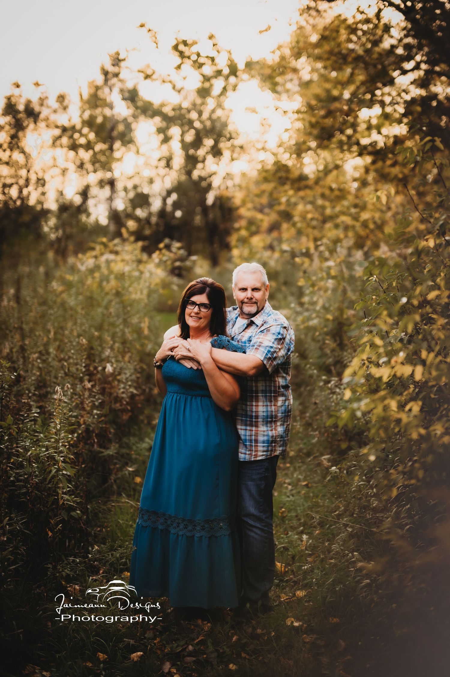Couple embracing in autumn forest setting during golden hour photography session.