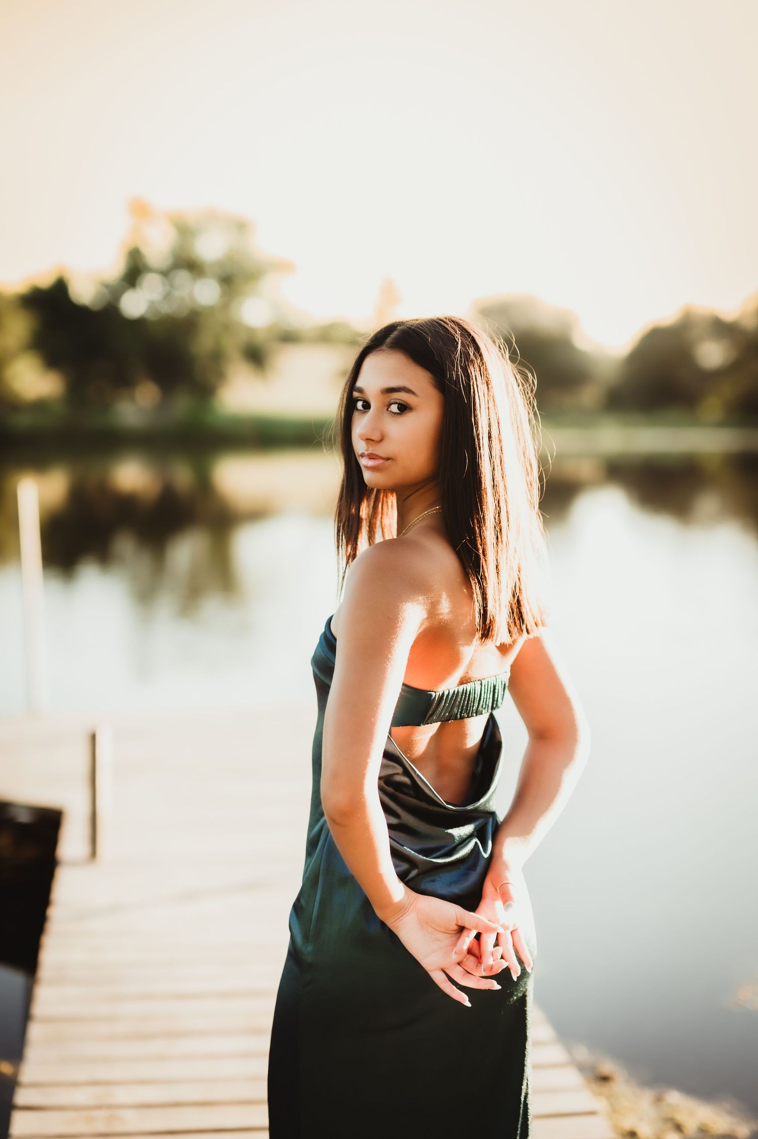 Woman in black tank top poses by tranquil lake at sunset creating artistic outdoor portraits in Boltonville, WI