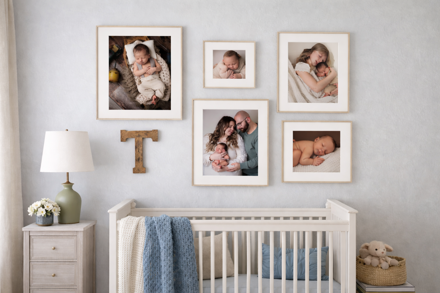 Nursery wall gallery with framed newborn and family photos above a white crib with blue blanket and wooden letter T.