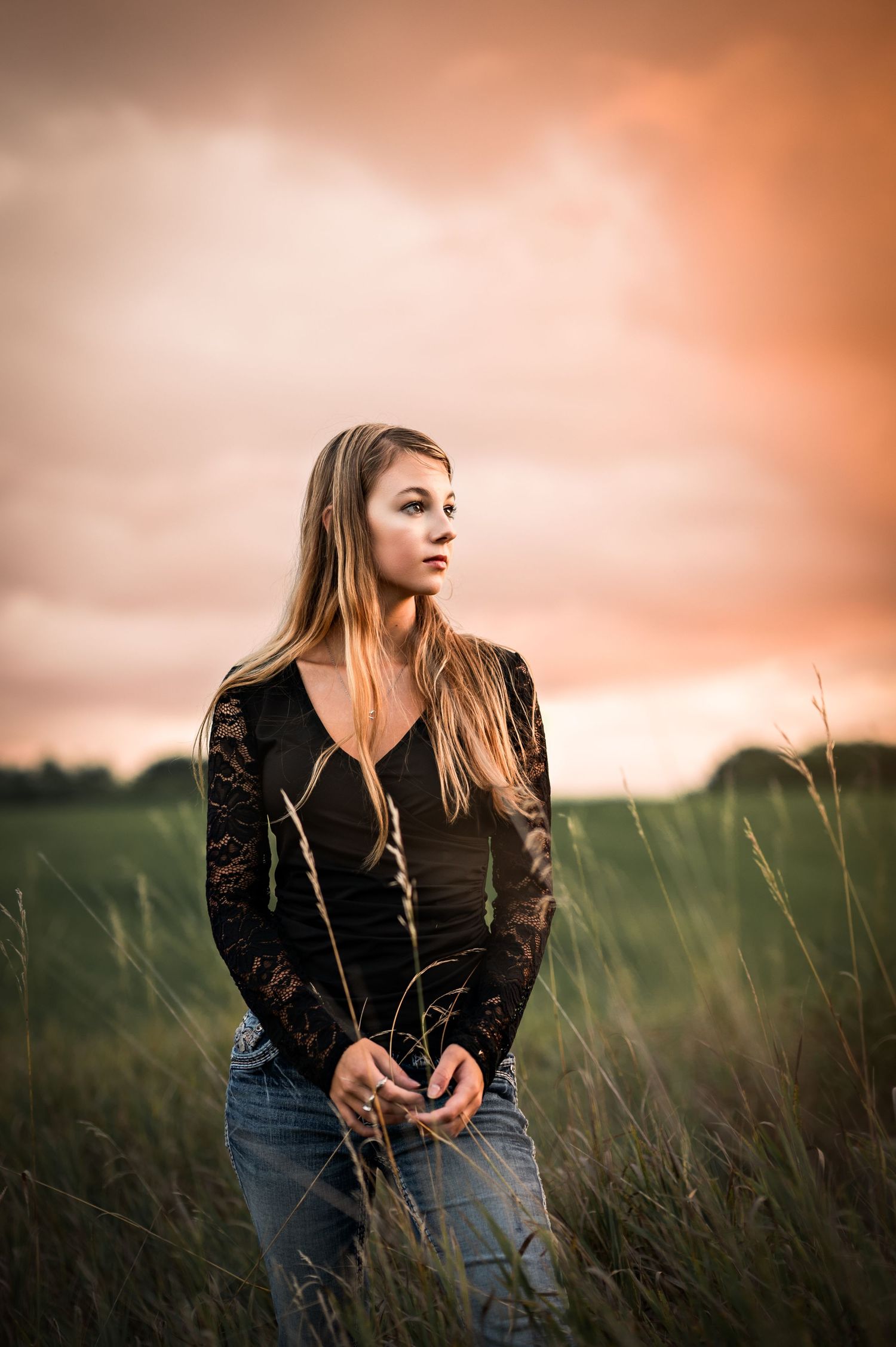 A person in a black leather jacket and jeans stands thoughtfully in a field of tall grass at sunset in Allenton, WI