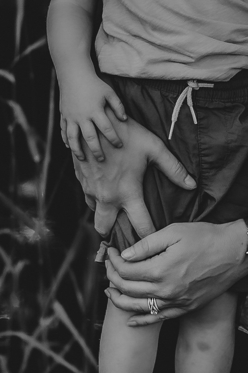Black and white close-up of hands touching, featuring a wedding ring detail.