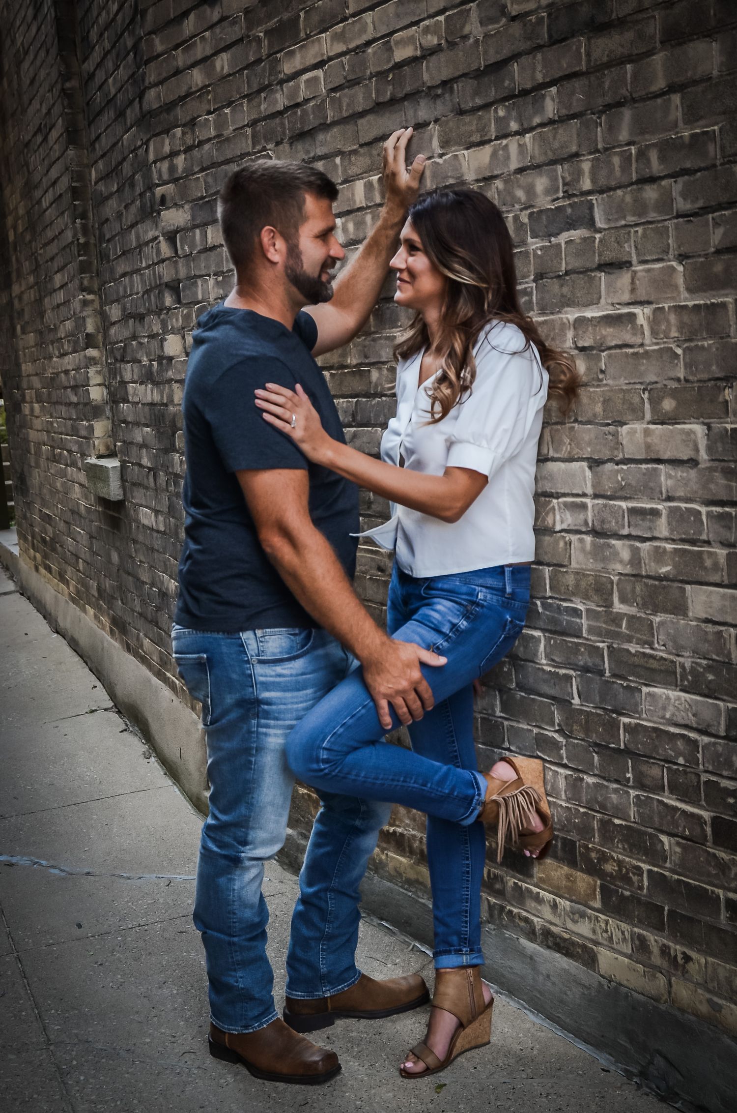 Romantic engagement photo session against a rustic brick wall showing intimate poses and casual attire.