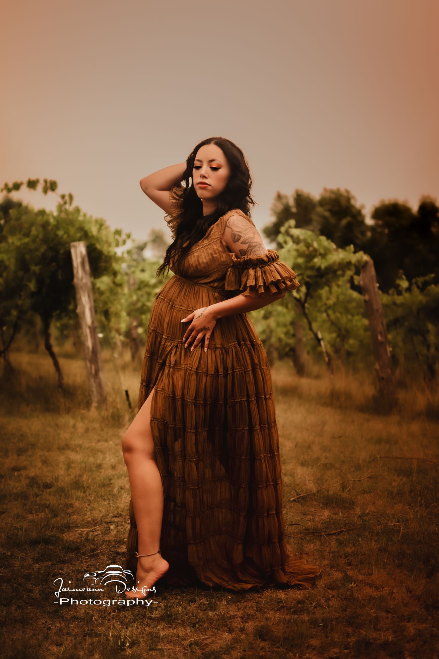 Elegant maternity portrait in a brown flowy dress against vineyard backdrop.
