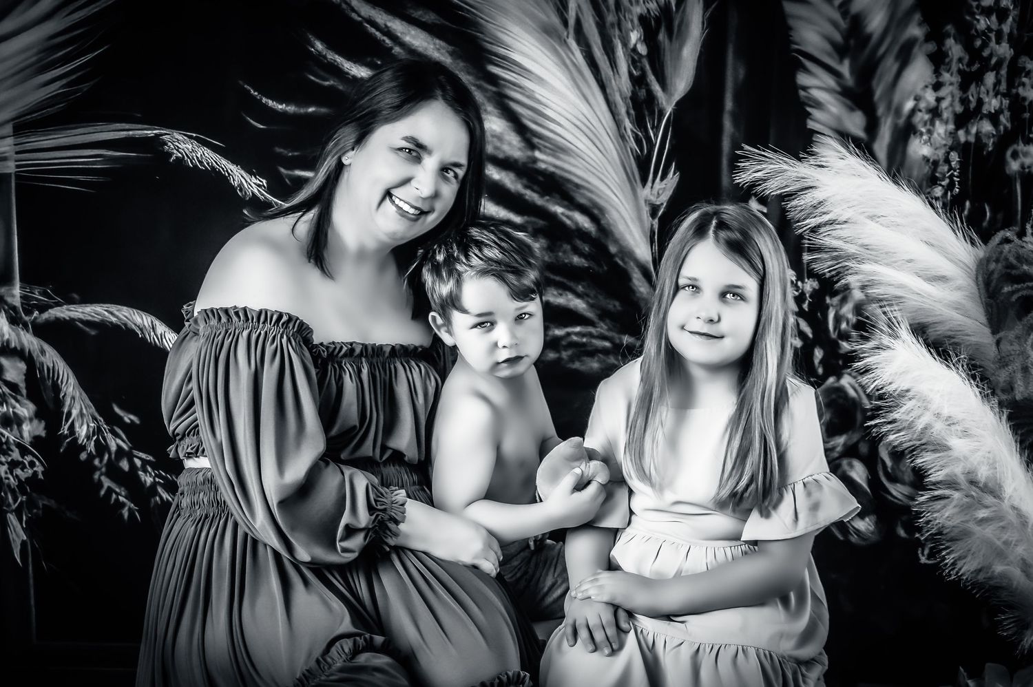 Family portrait with stylish off-shoulder dresses against dark tropical background.