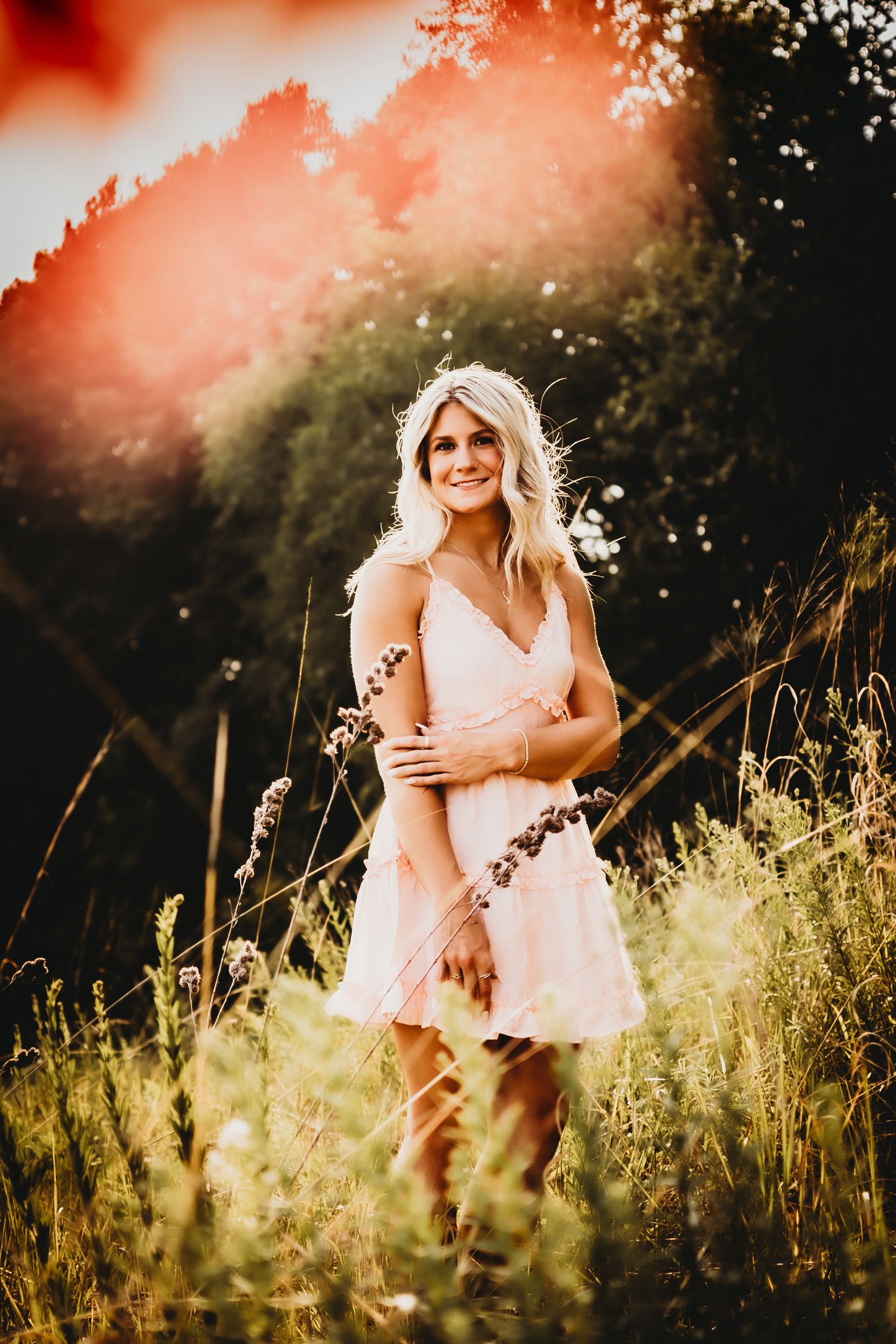 Person in pink dress stands in golden sunlit meadow during sunset.