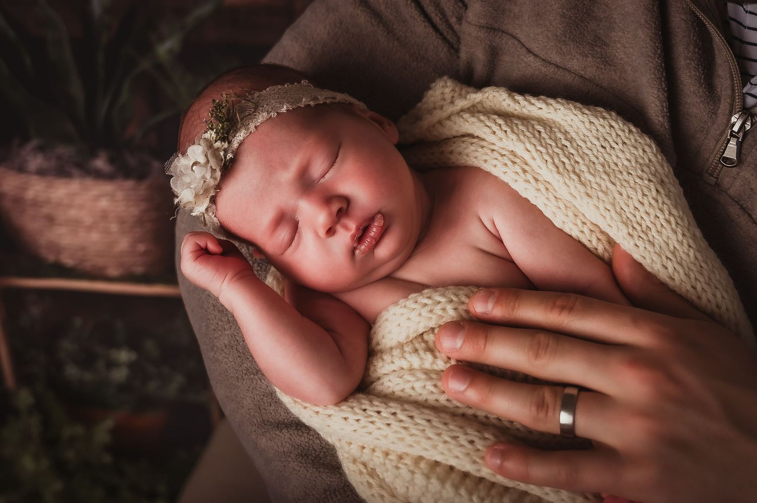 Sleeping newborn with lace headband wrapped in cream knit blanket.
