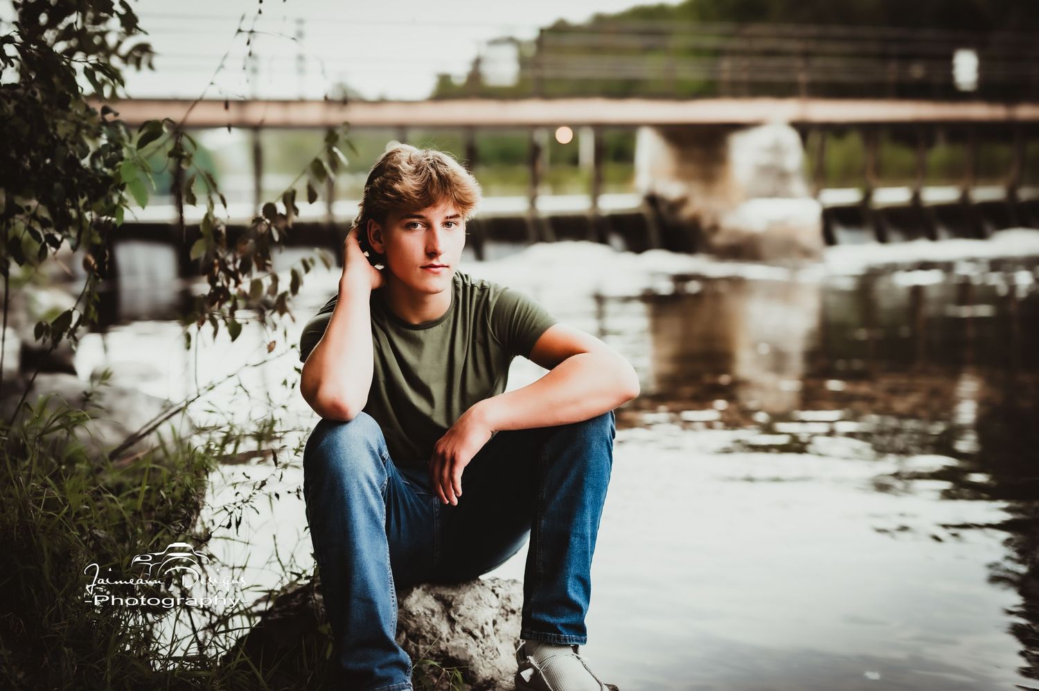 Person sitting on rocks by water with bridge visible in background.