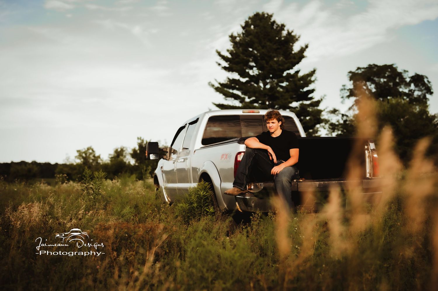 White pickup truck parked in tall grass field during golden hour.