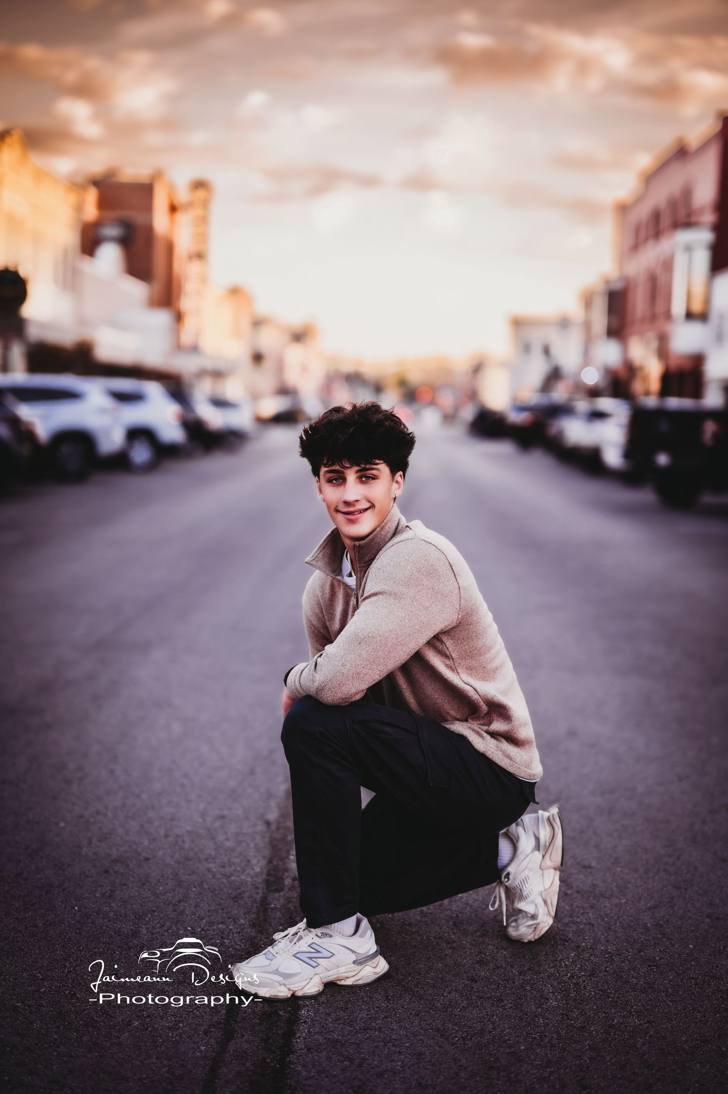 Street fashion portrait at sunset with person in beige sweater crouching on urban road.