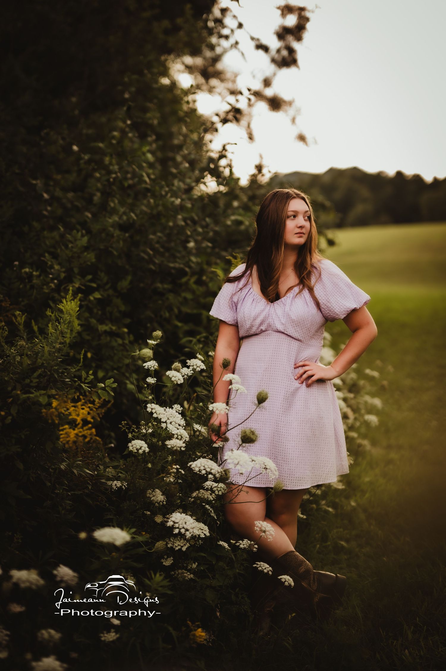 Portrait in pink dress beside flowering bushes on landscaped grounds.