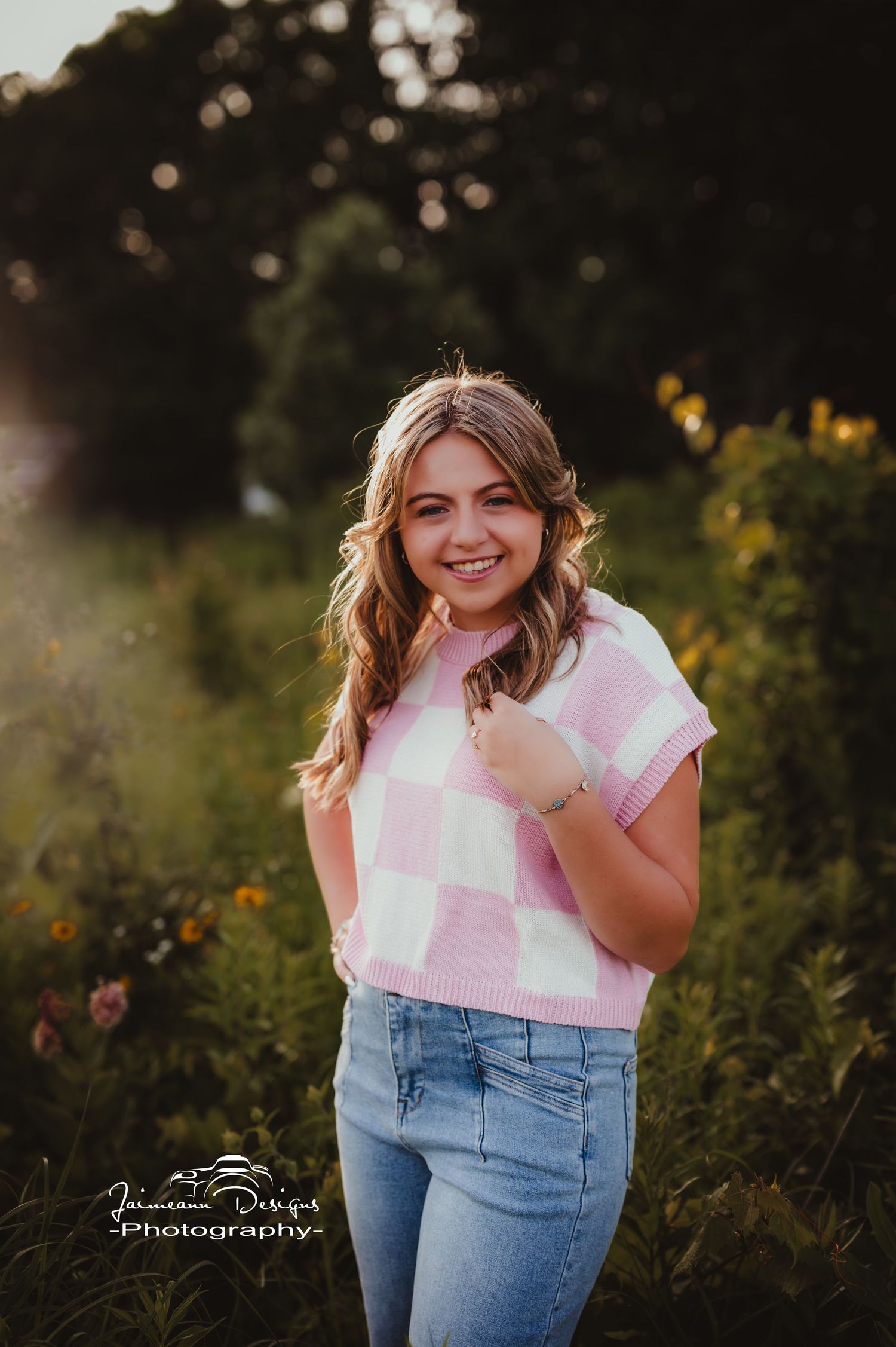 Outdoor portrait in pink and white checkered top with jeans among wildflowers.