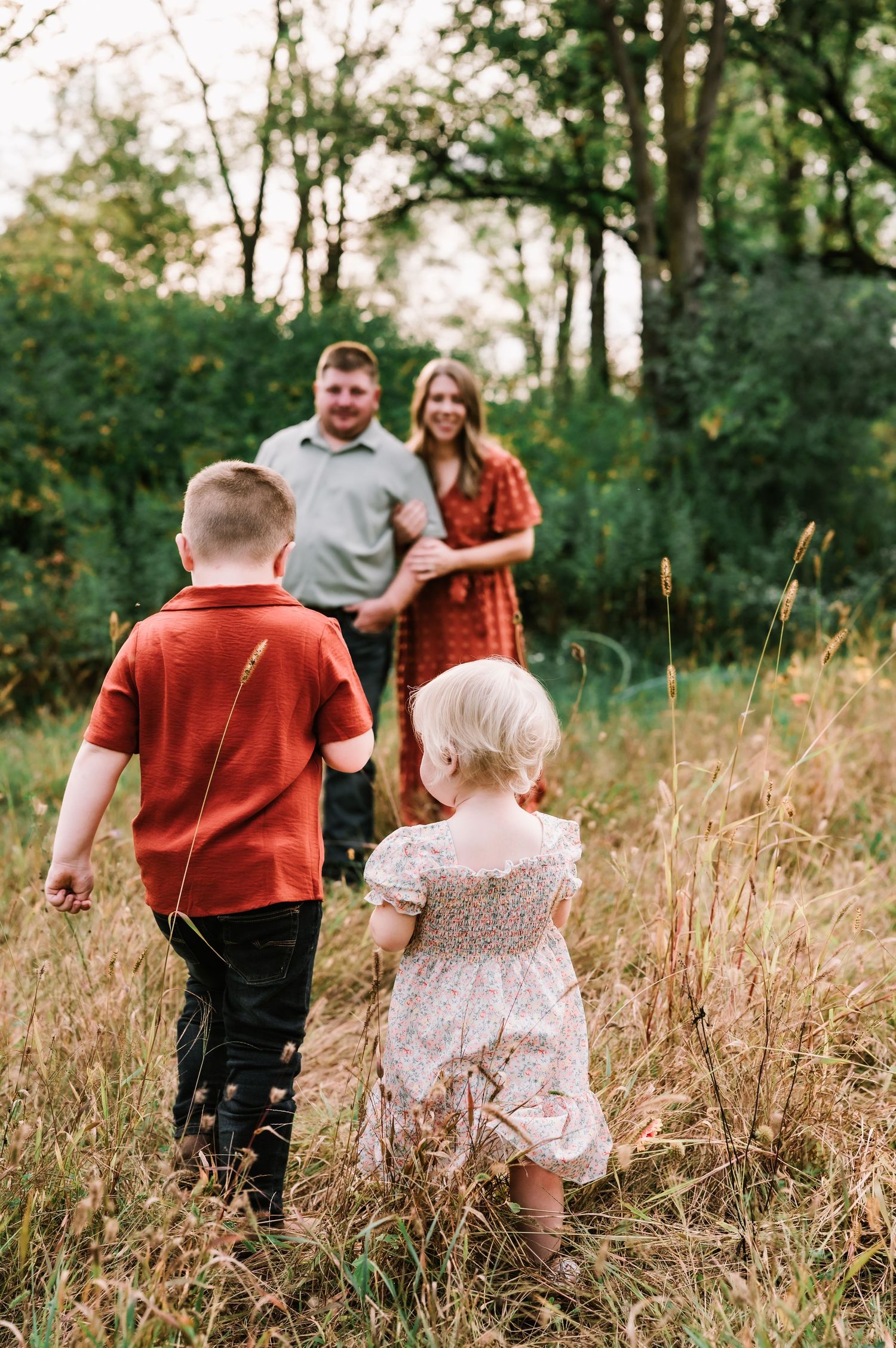 A family walks through a field of tall golden grass during a sunset photo session in nature.