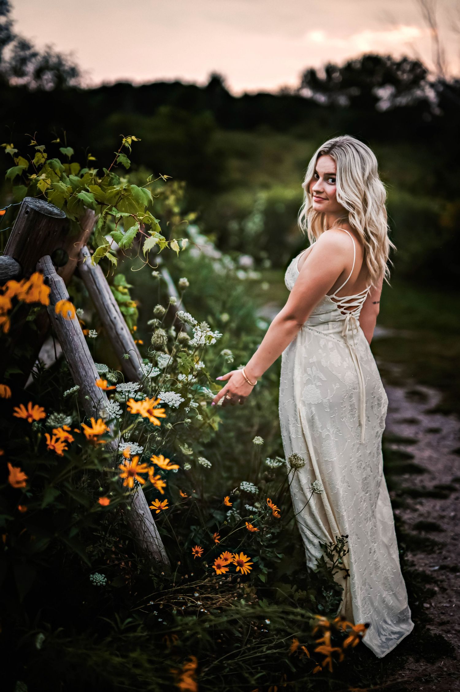 A person in a white dress poses among orange lilies and wildflowers in a garden at dusk in Menomonee Falls, WI Park
