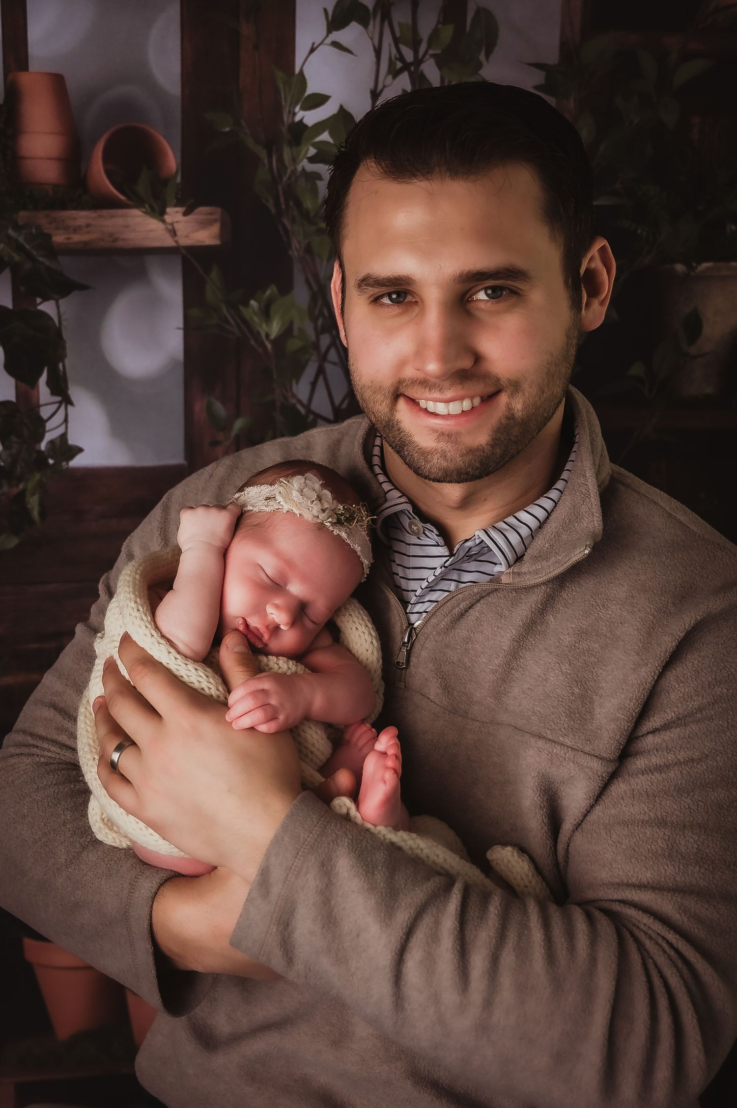 Warm portrait of newborn swaddled in cream blanket being held against brown sweater.