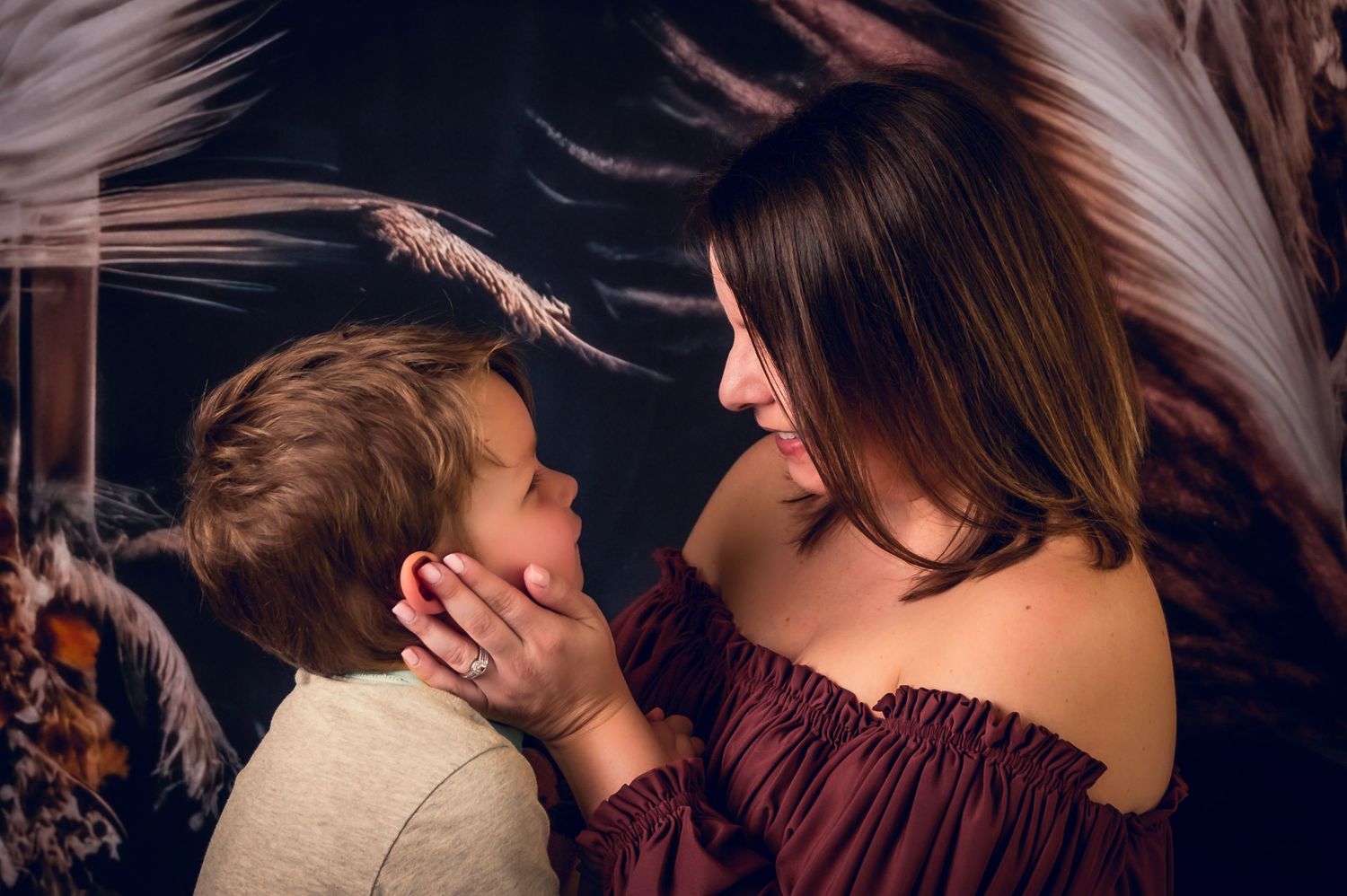 Tender moment captured in portrait against dramatic feather backdrop.