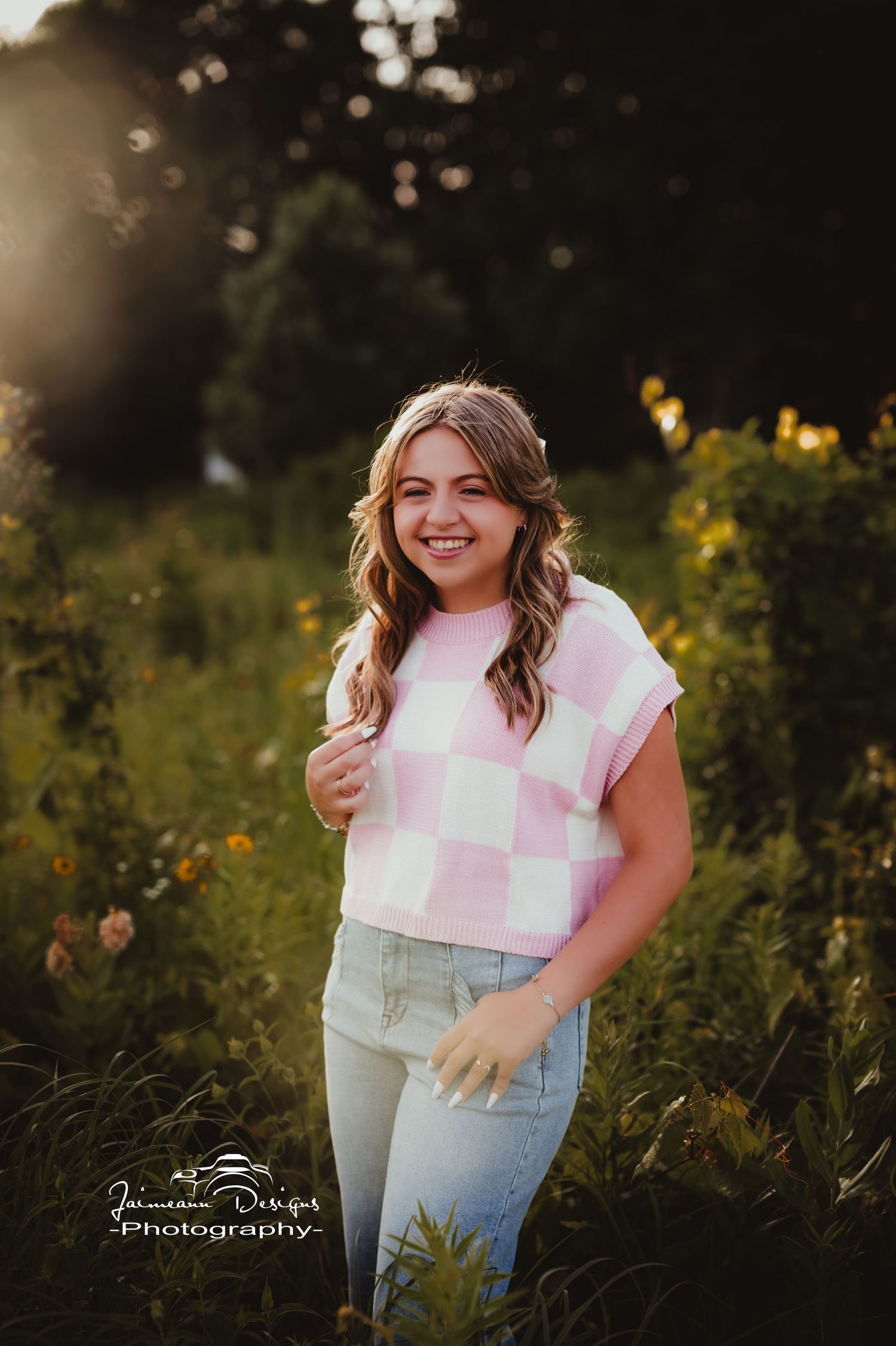 Portrait in a wildflower field at golden hour wearing pink checkered top and jeans.