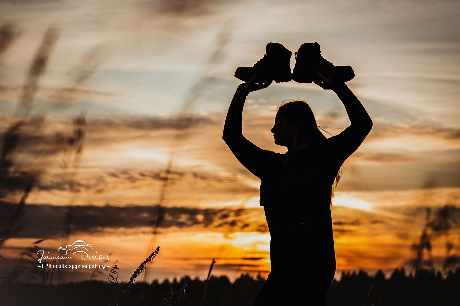 Silhouette holding boots against dramatic sunset sky.
