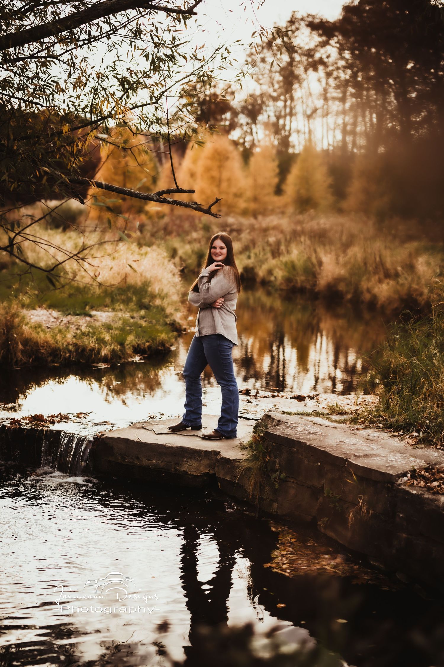 Person standing on stone ledge by reflective pond during golden hour.