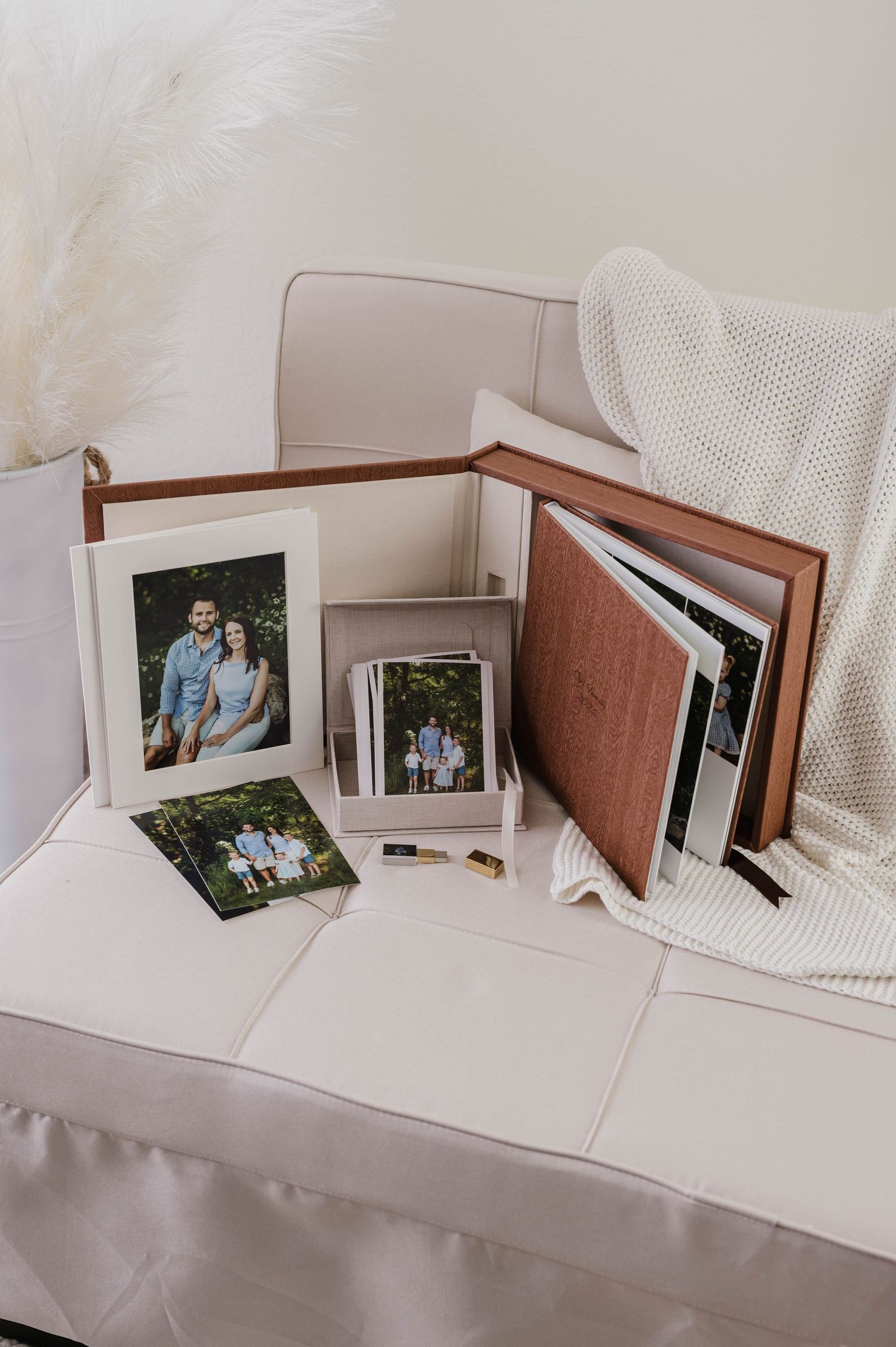 Elegant family photo display with framed portraits, photo box, and leather album arranged on a cream sofa.