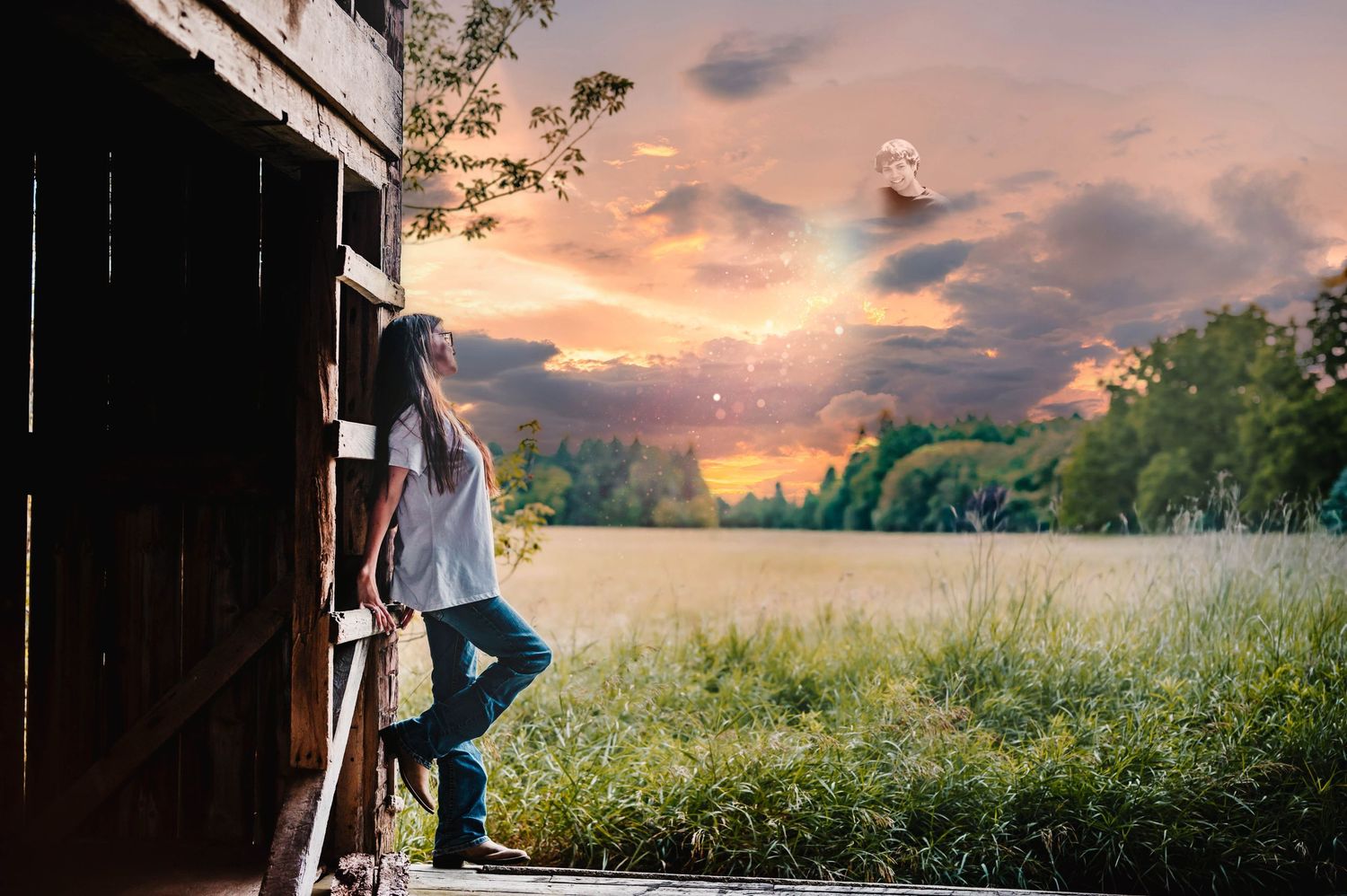 A young woman in jeans leans against a rustic barn doorway overlooking a golden field at sunset.