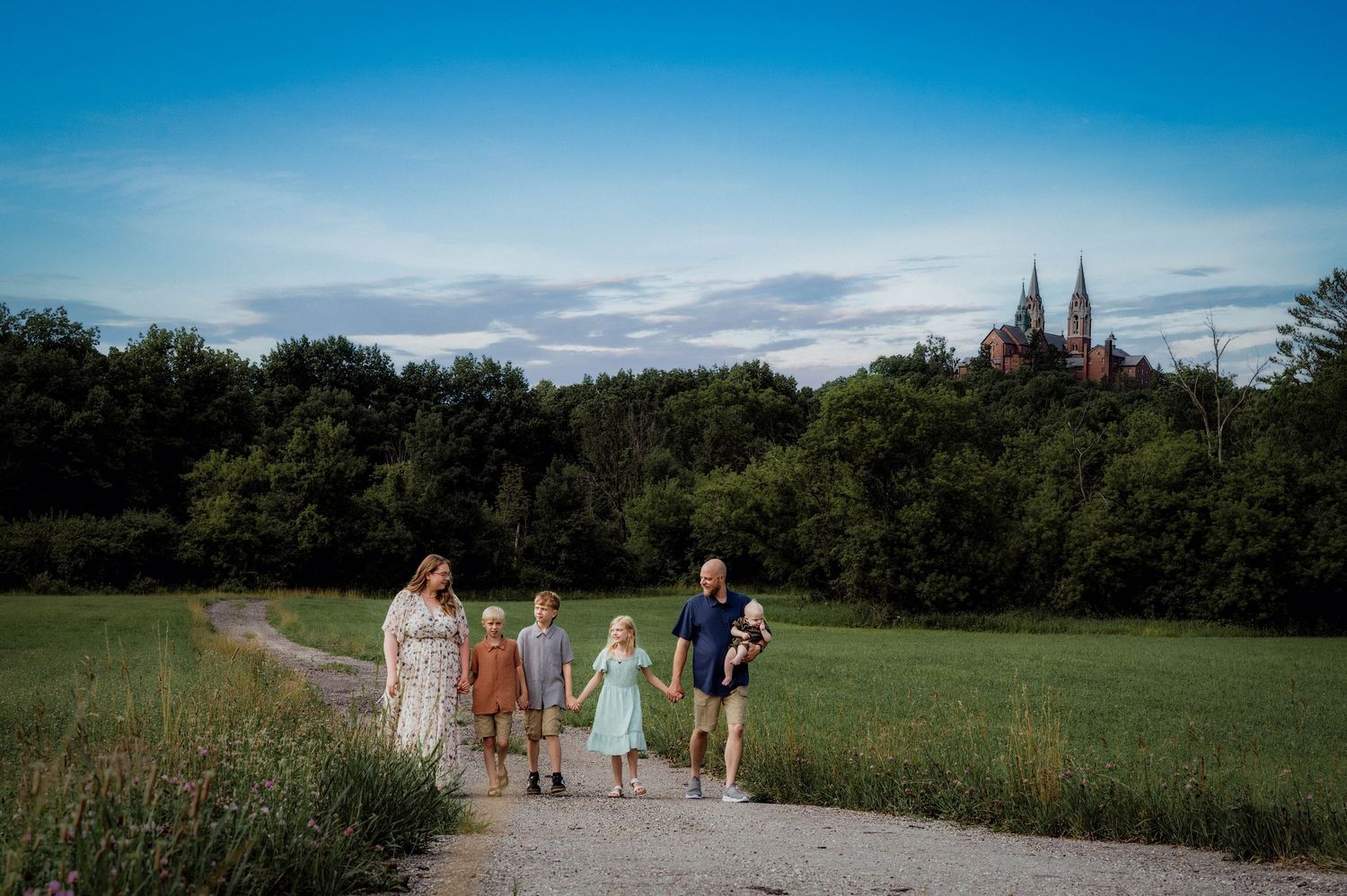 Holly Hill Basilica, WI. Family of five walking on a scenic path through green fields with a historic church visible in the background.