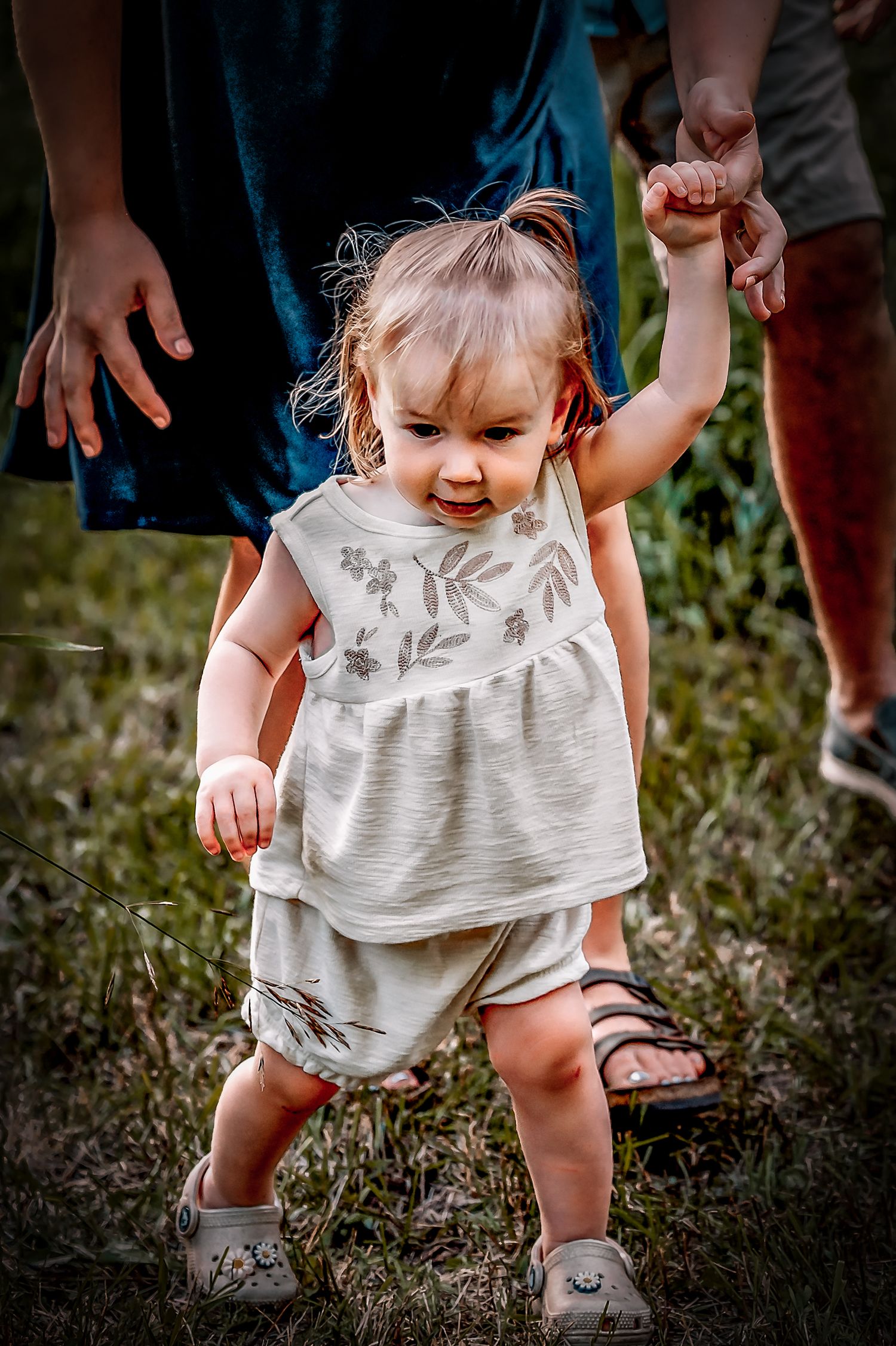 Small child wearing a ruffled white top and sandals plays outdoors in a grassy area near Grafton, WI