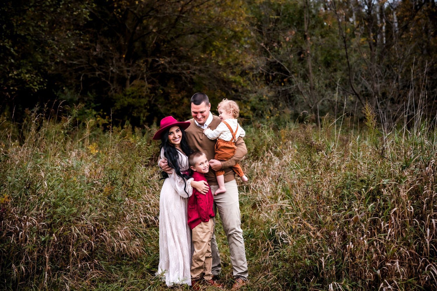 A family stands together in a sunlit autumn meadow surrounded by tall grass and trees in the background at private outdoor studi in Wisconsi