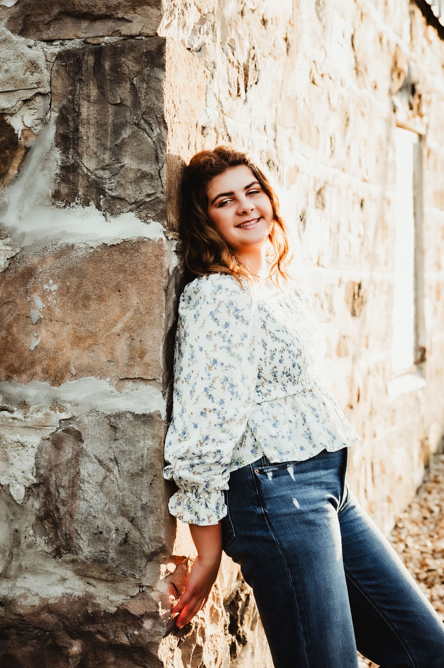 Casual portrait against a rustic stone wall in a floral print top and jeans.