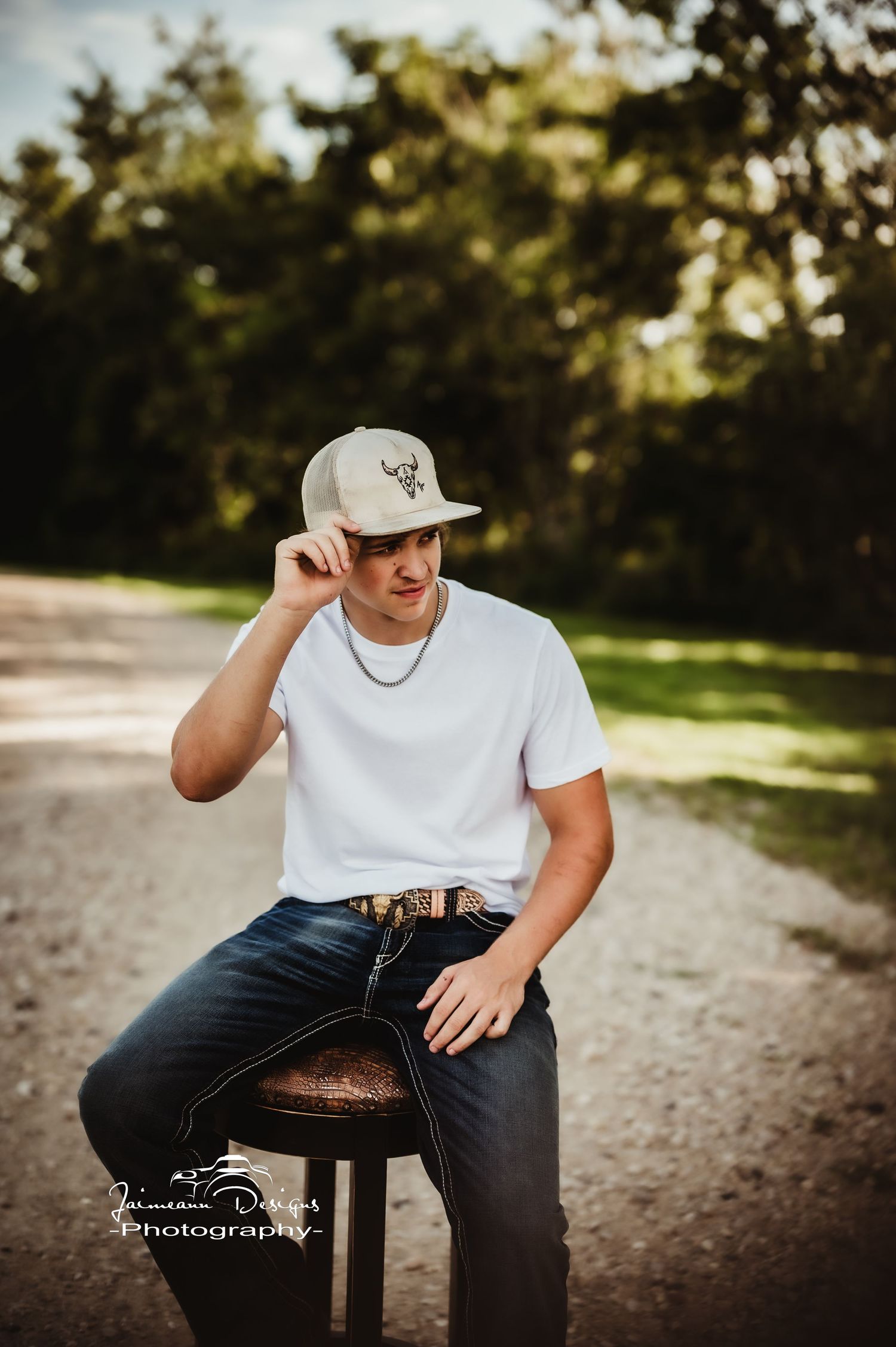 Casual outdoor portrait on wooden stool with baseball cap and white t-shirt.