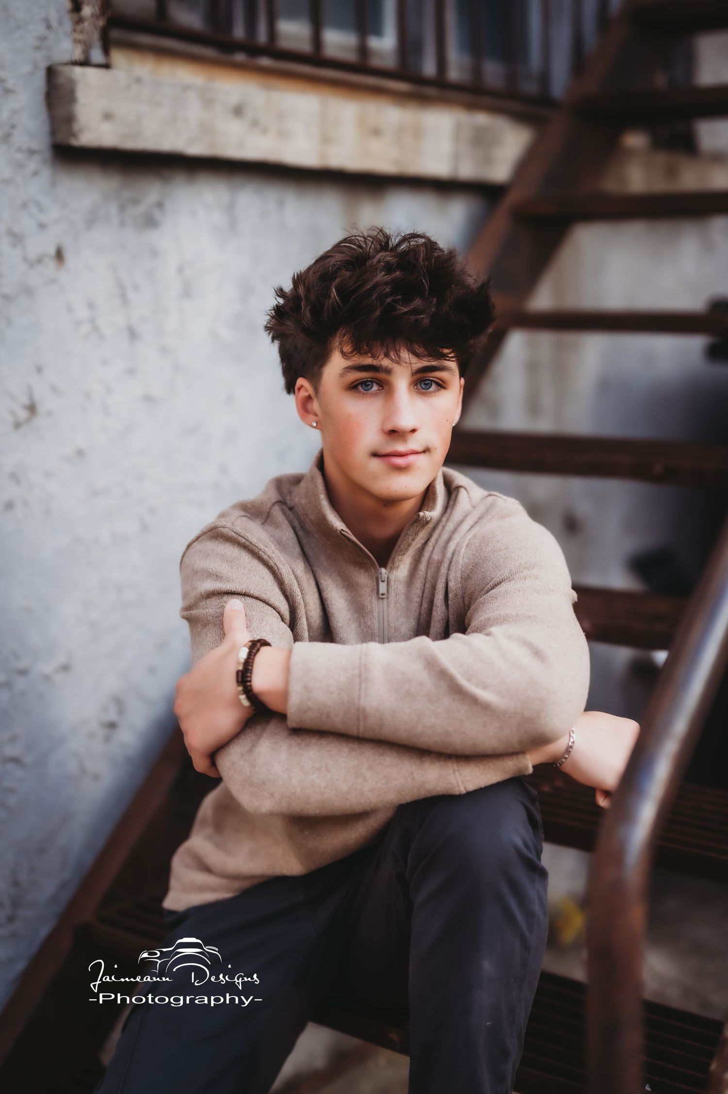 Urban lifestyle portrait near metal stairs featuring tan pullover and casual styling.