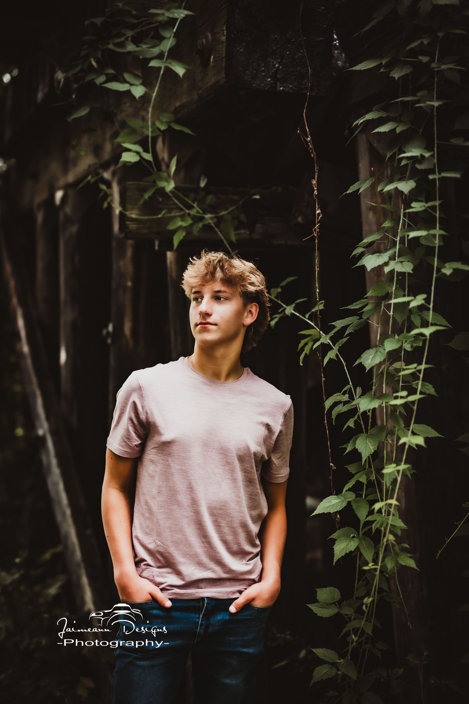 Person in pink t-shirt standing against wooded background with vines.